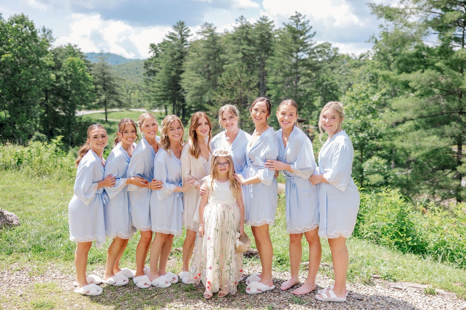 Bridal party in light blue robes poses together on mountain overlook.