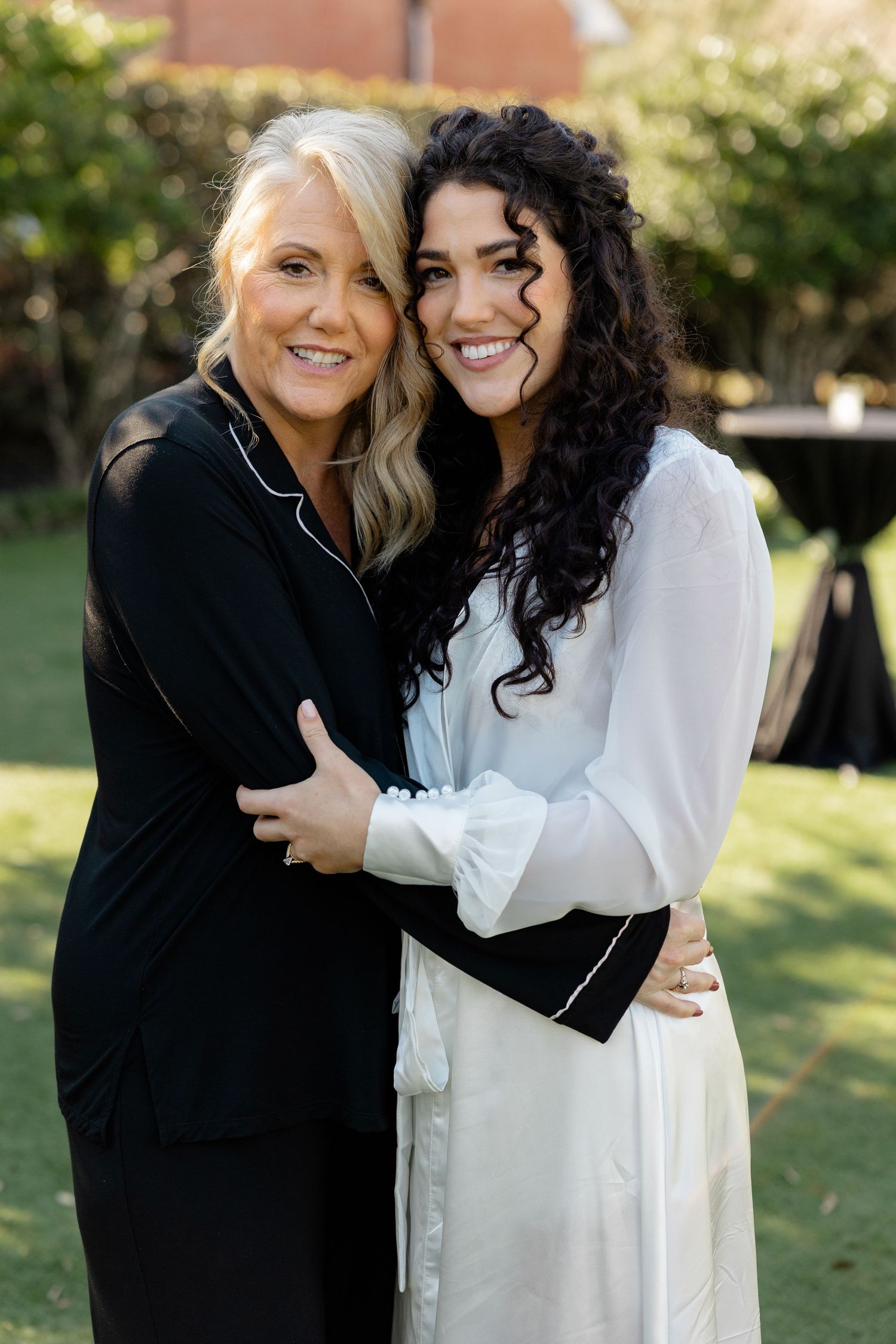 Two women sharing a warm embrace and smiling together in an outdoor garden setting.