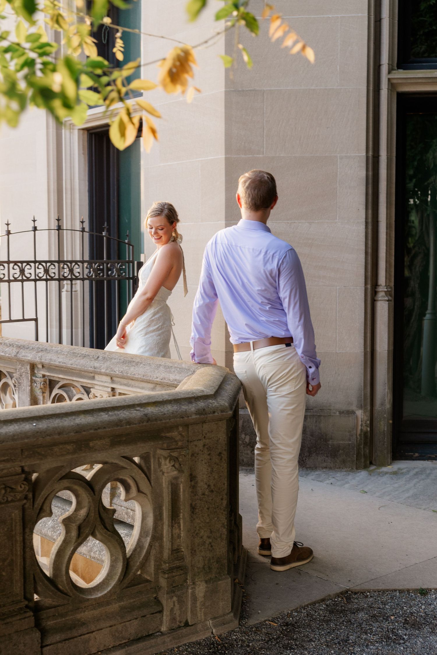 Couple in white and purple attire standing together on an ornate stone balcony at a historic estate.