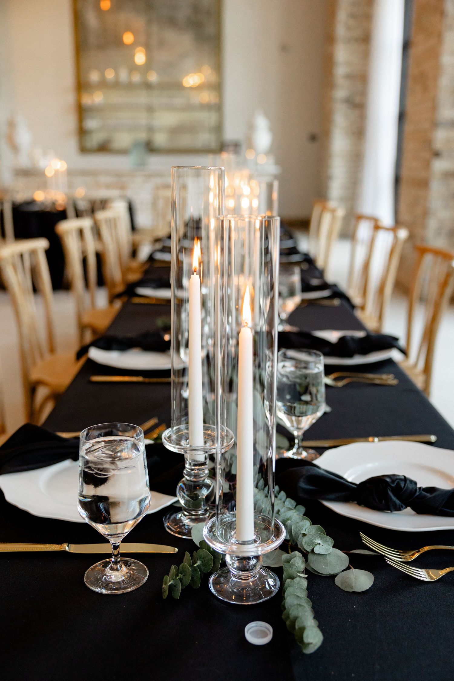 Elegant wedding table setting with tall glass candleholders, black tablecloths, and white place settings.