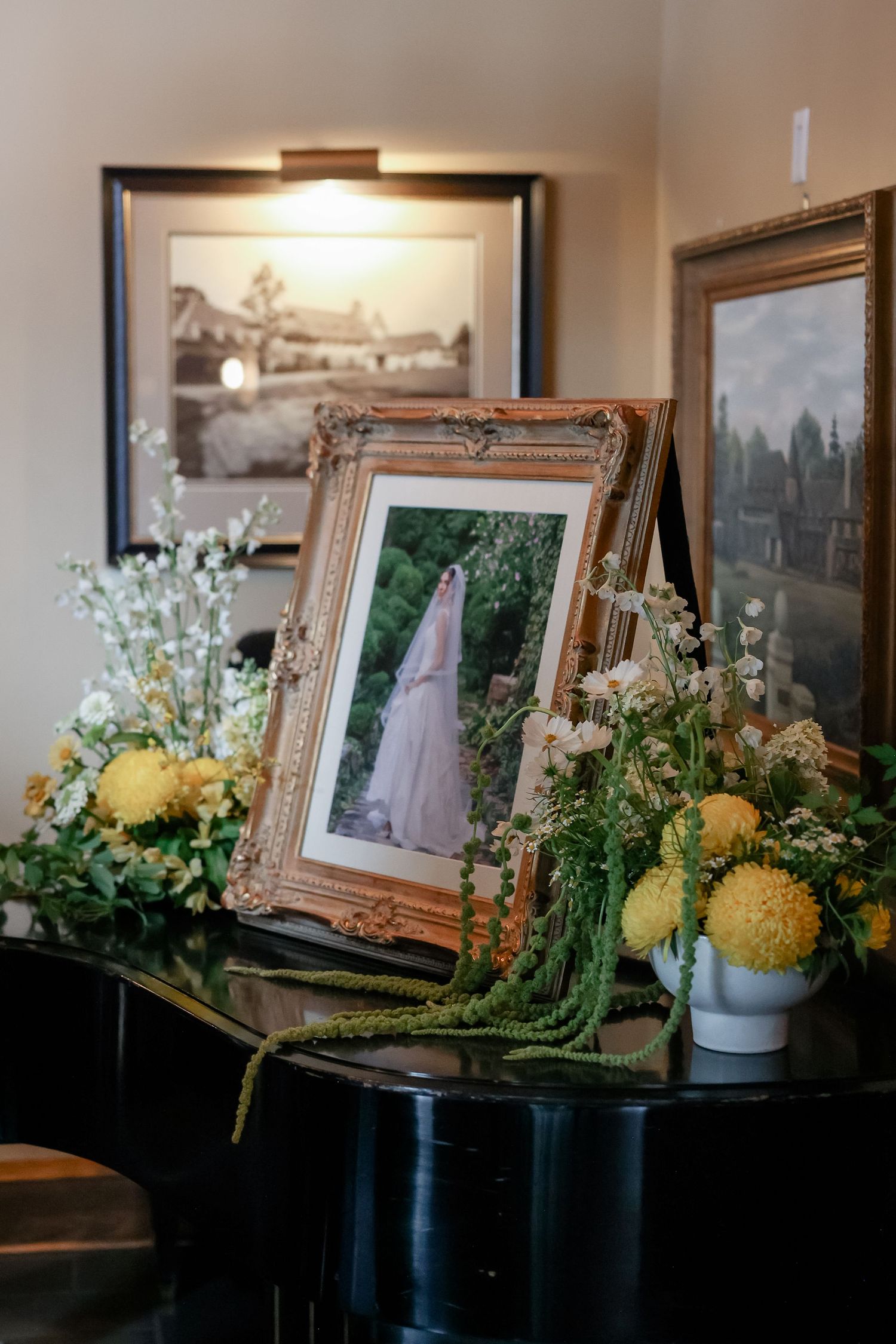 Ornate gold-framed bridal portrait on piano surrounded by yellow and white floral arrangements with greenery.