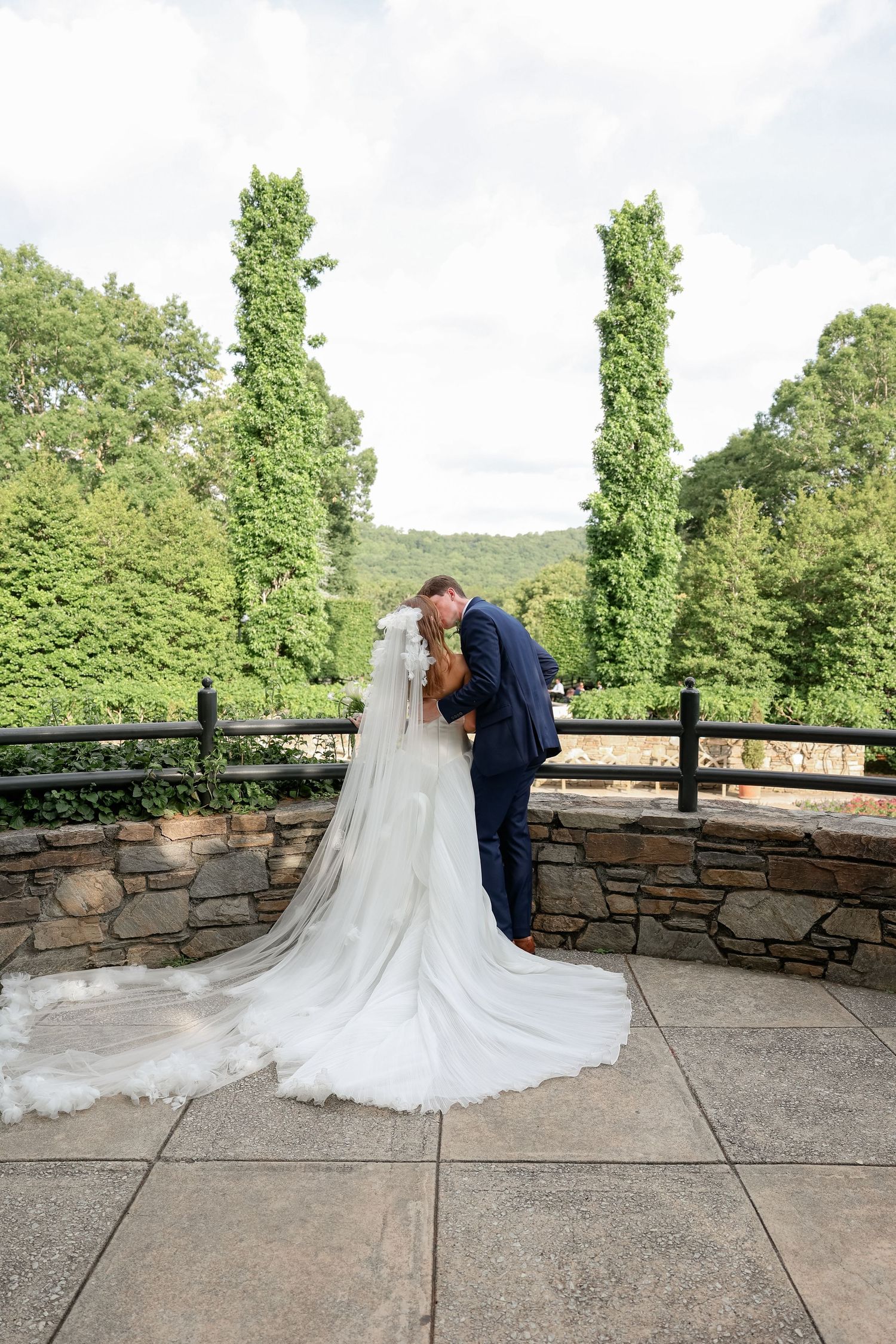 Wedding couple embracing on stone patio with dramatic train of white dress.