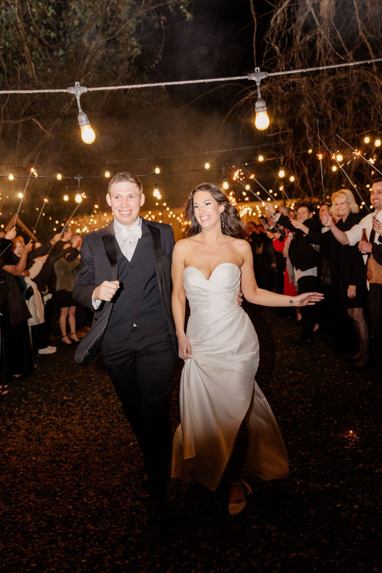 Wedding celebration under string lights at night with guests dancing outdoors.