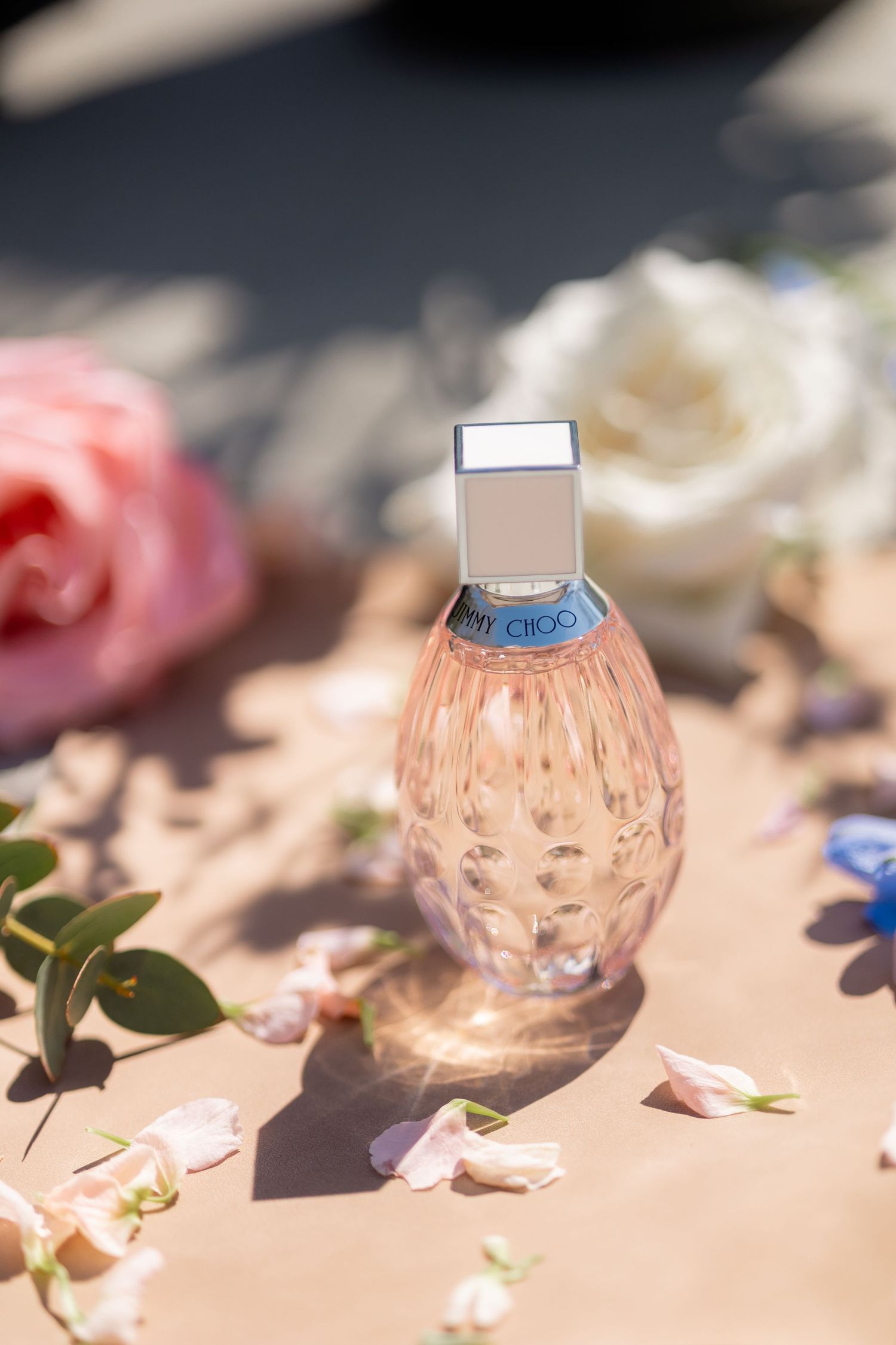 Decorative glass perfume bottles sit elegantly among scattered rose petals in warm light.