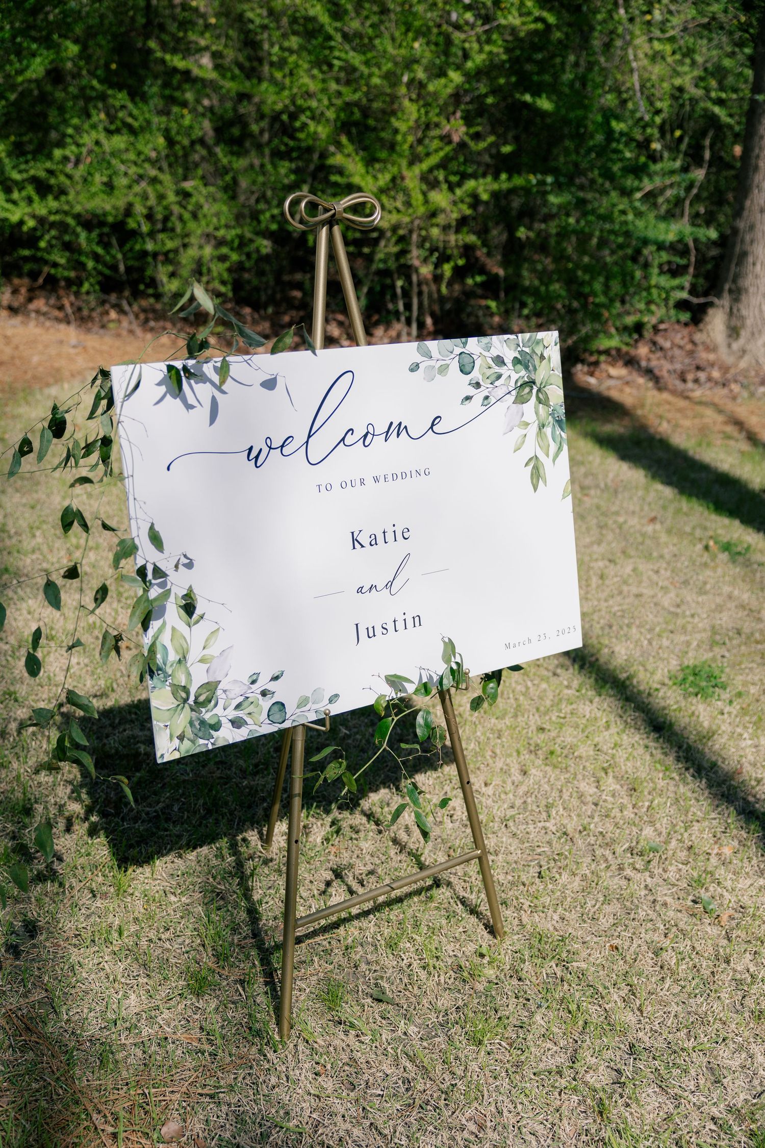Elegant wedding welcome signs with greenery details displayed on wooden stakes in a garden setting.