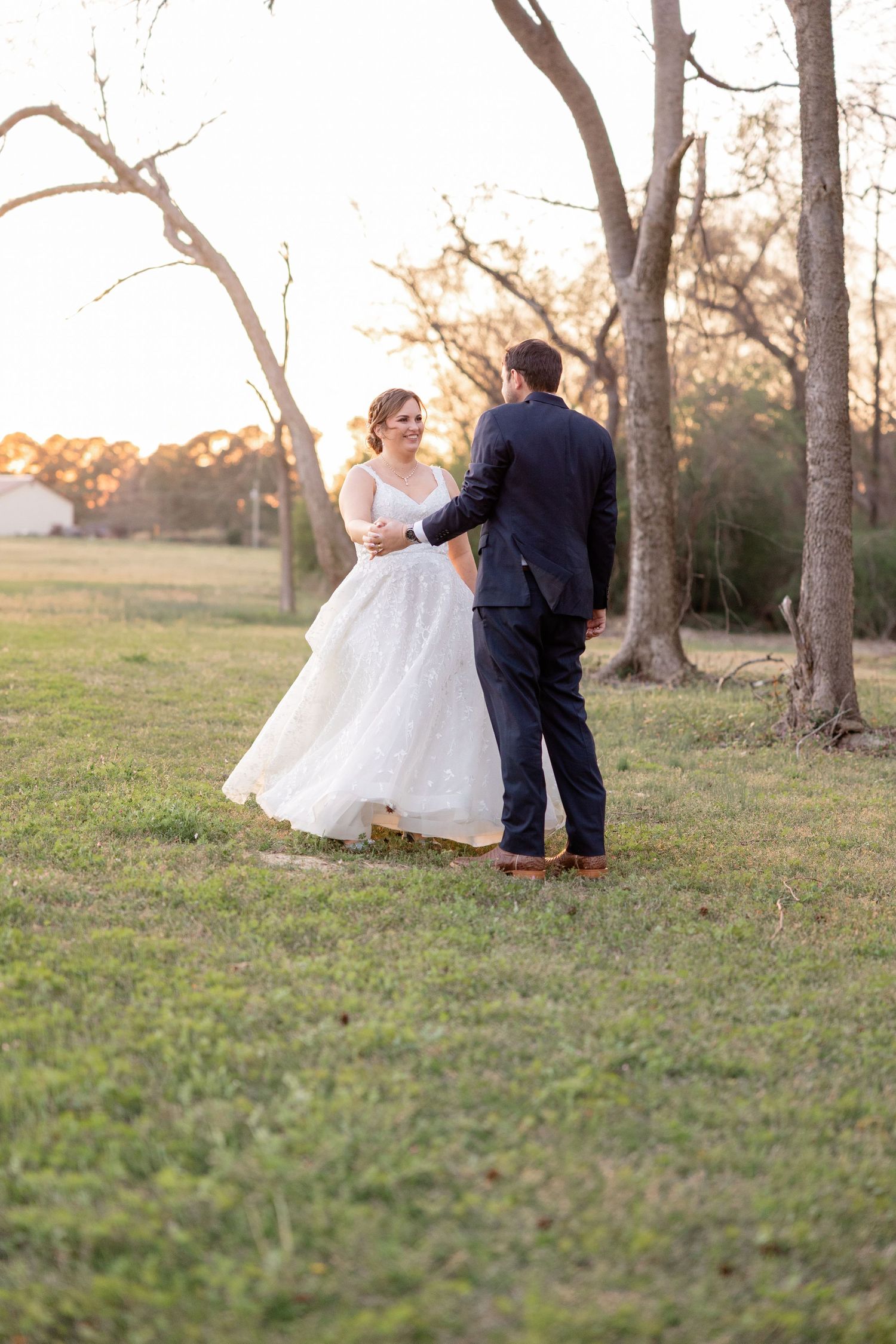 A couple share a romantic moment at sunset in a field with bare trees in the background.
