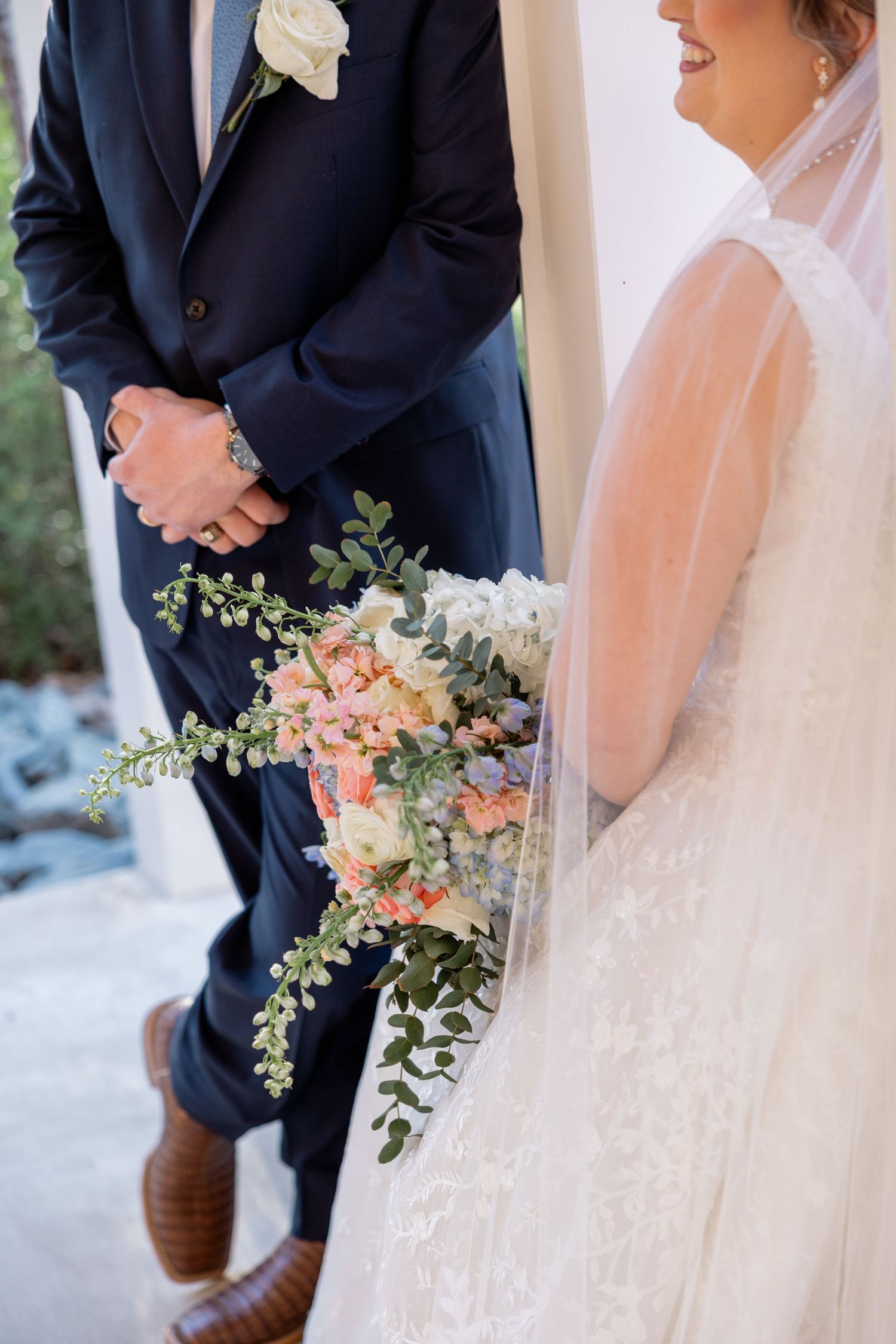 Close-up of wedding bouquet with peach roses and cascading greenery against white bridal veil.