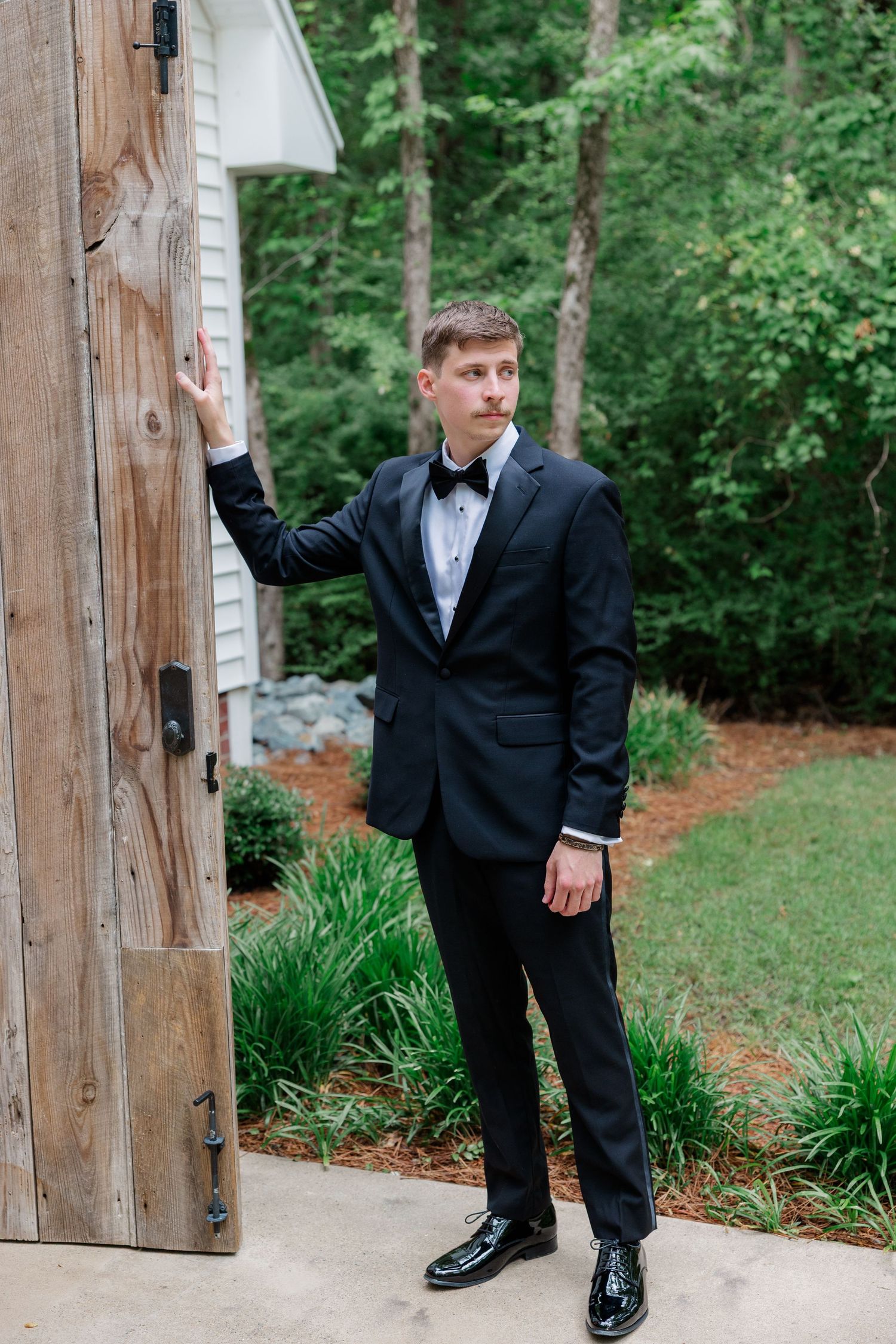 Classic wedding photography poses with formal attire by wooden beams and greenery.