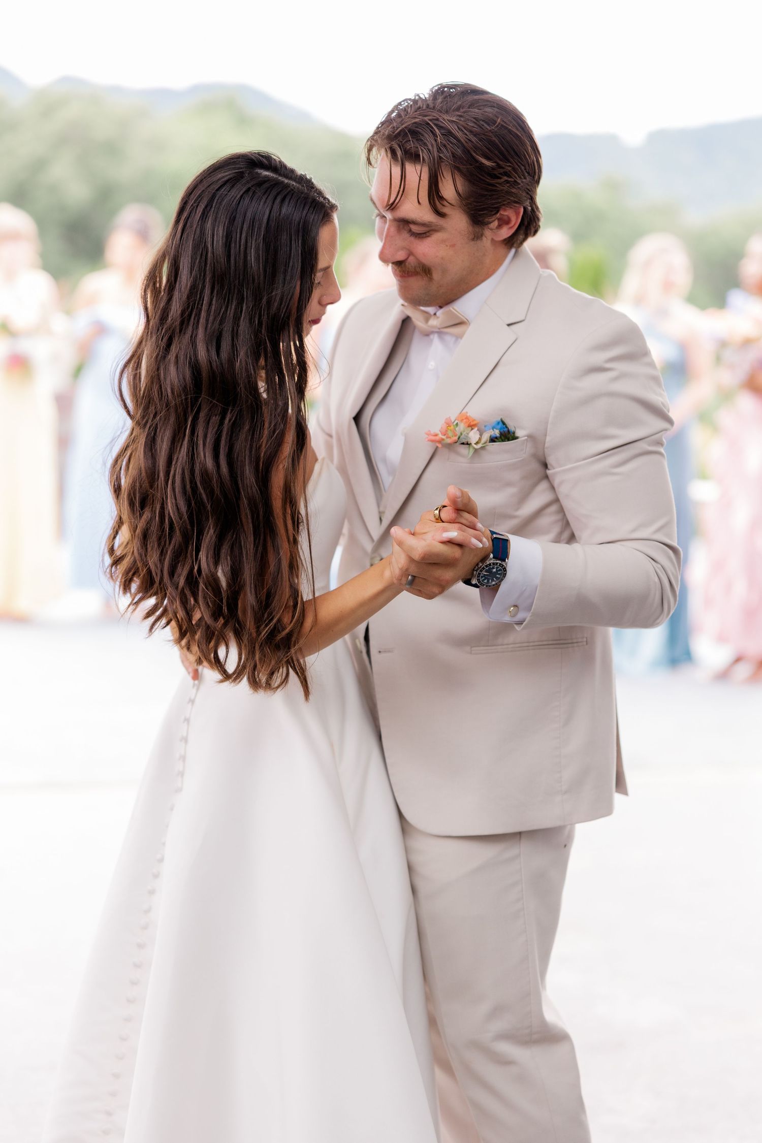 Couple in white attire dancing together on a beach.