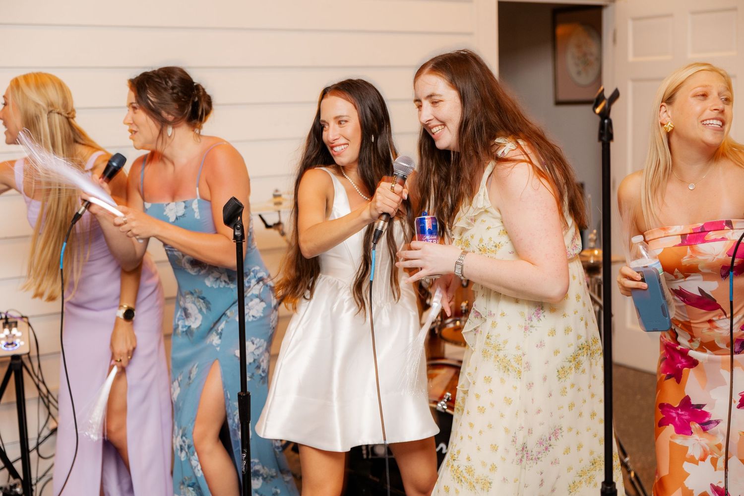 Wedding party members in pastel dresses sing and dance together during reception celebrations.