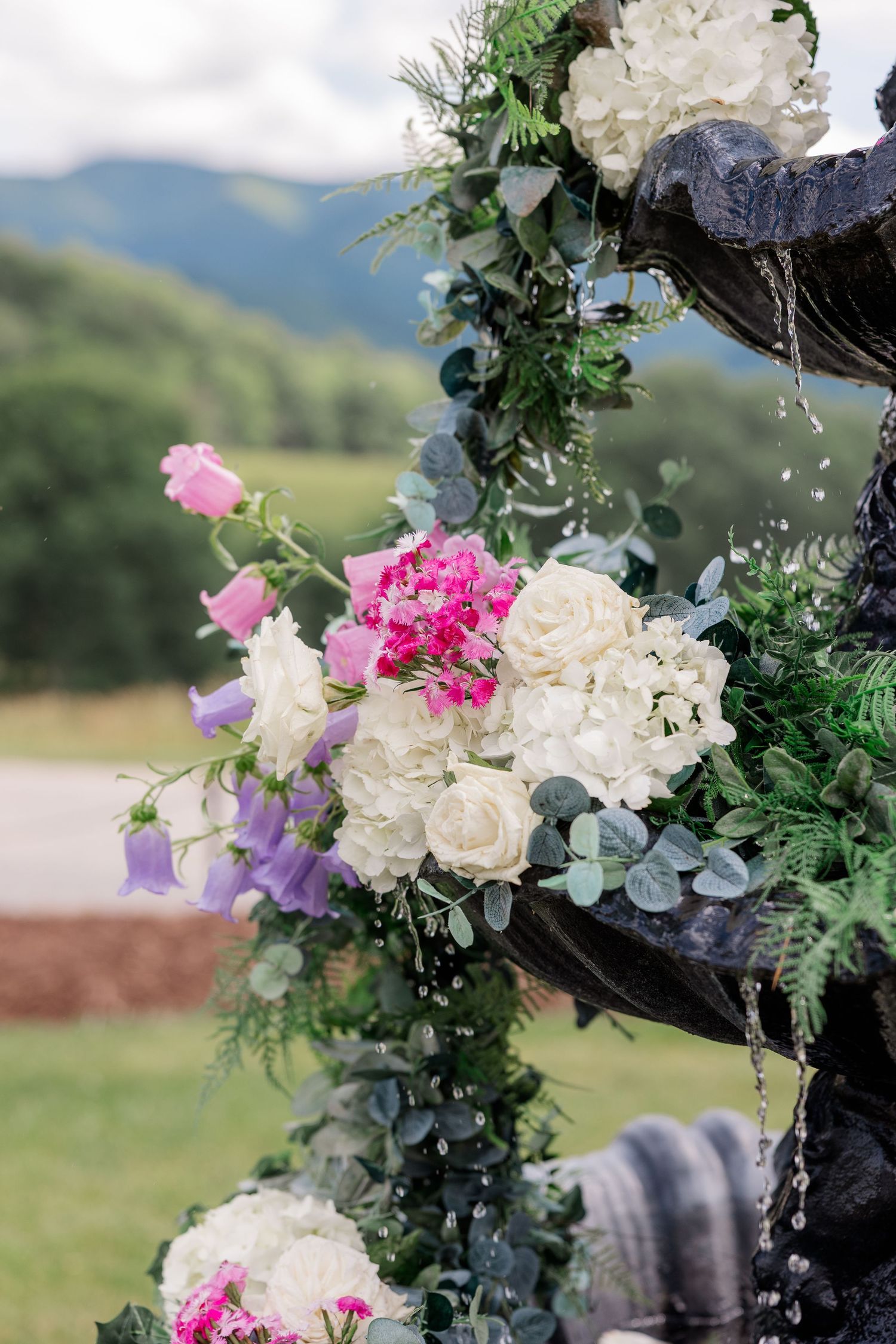 Floral wedding arch decorated with white roses, pink flowers and purple blooms against a mountain backdrop.