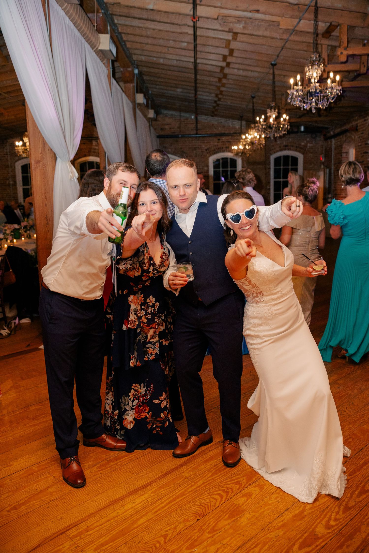 Bride in sunglasses and groom celebrate with guests on the dance floor at their wedding reception.