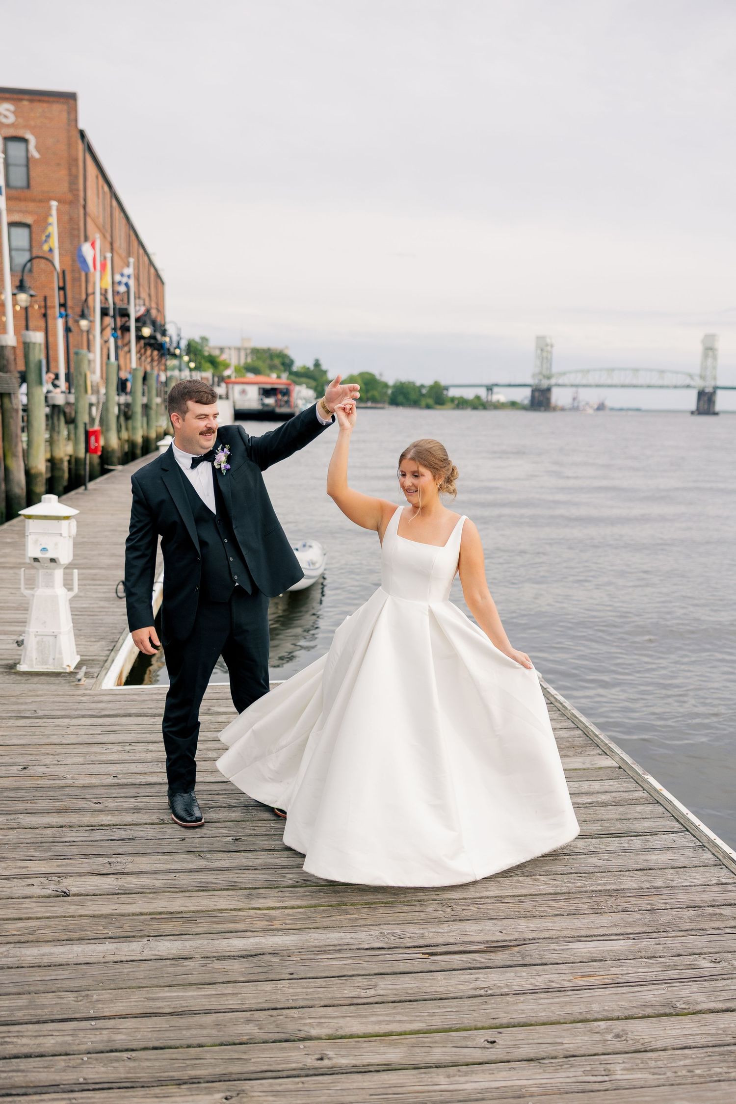 Bride and groom dancing on a waterfront dock, with the bride in a white ballgown and groom in a black tuxedo.
