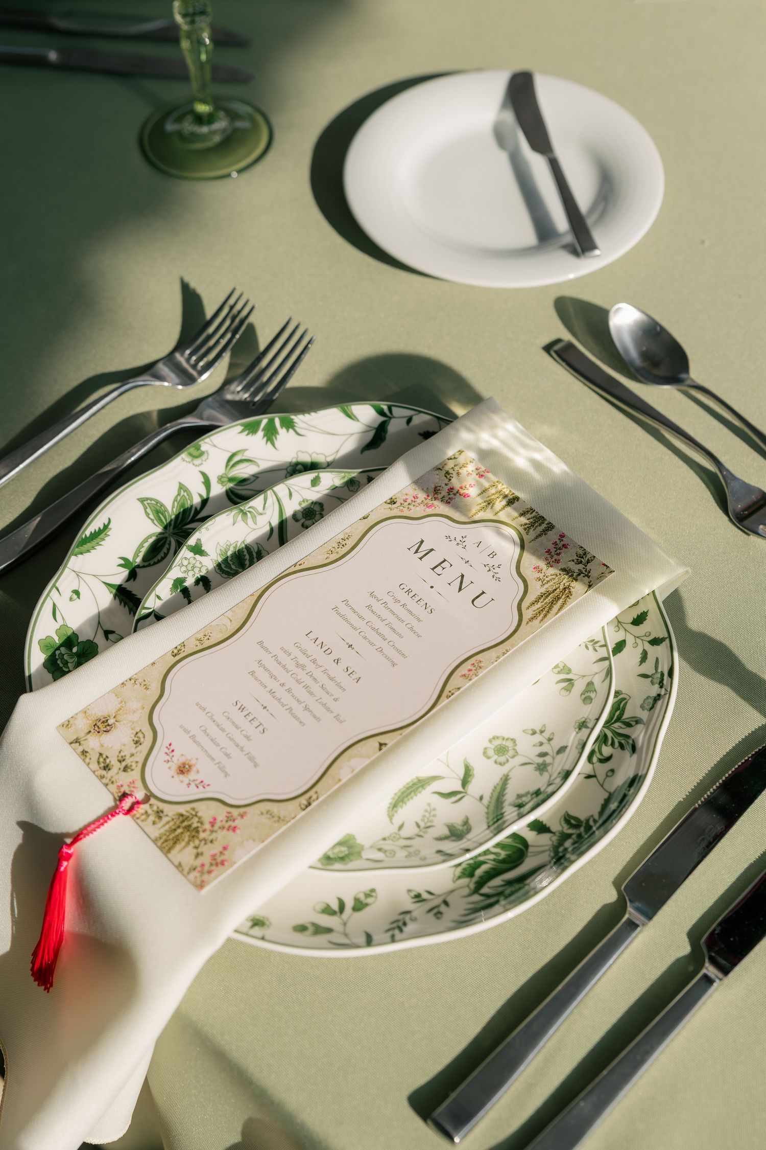 Elegant wedding place setting with green botanical china, menu card, and dark silverware.