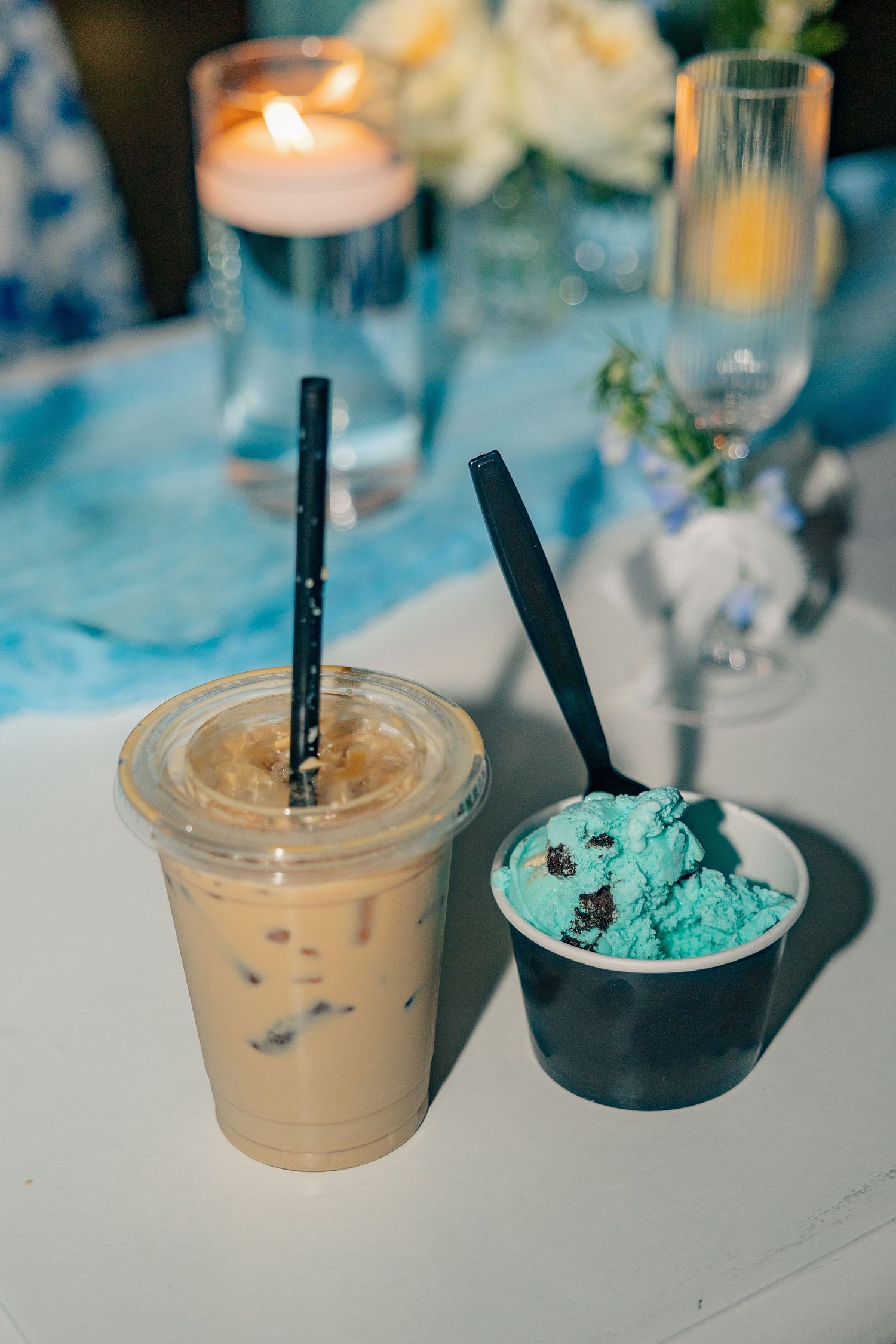 Wedding reception dessert table with iced coffee and blue mint ice cream cup beside candles and florals.