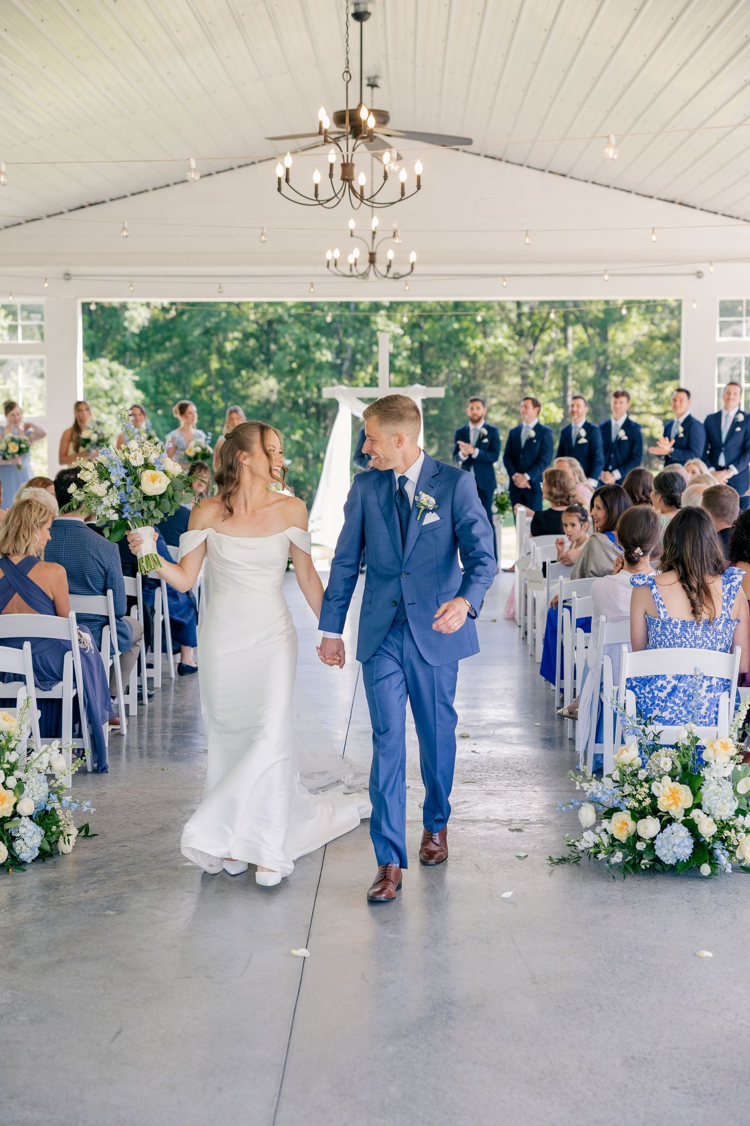 Newlyweds walk down aisle hand in hand after wedding ceremony in elegant white pavilion venue.