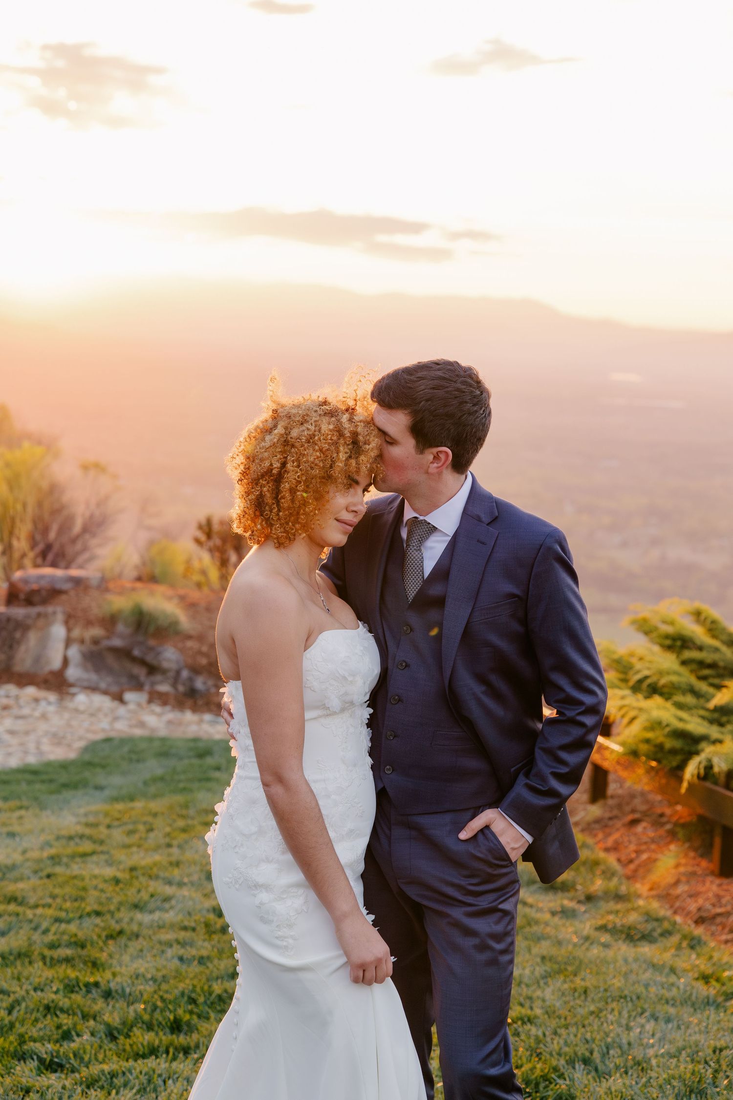 Bride and groom share intimate sunset moment on hilltop with golden mountain valley backdrop.