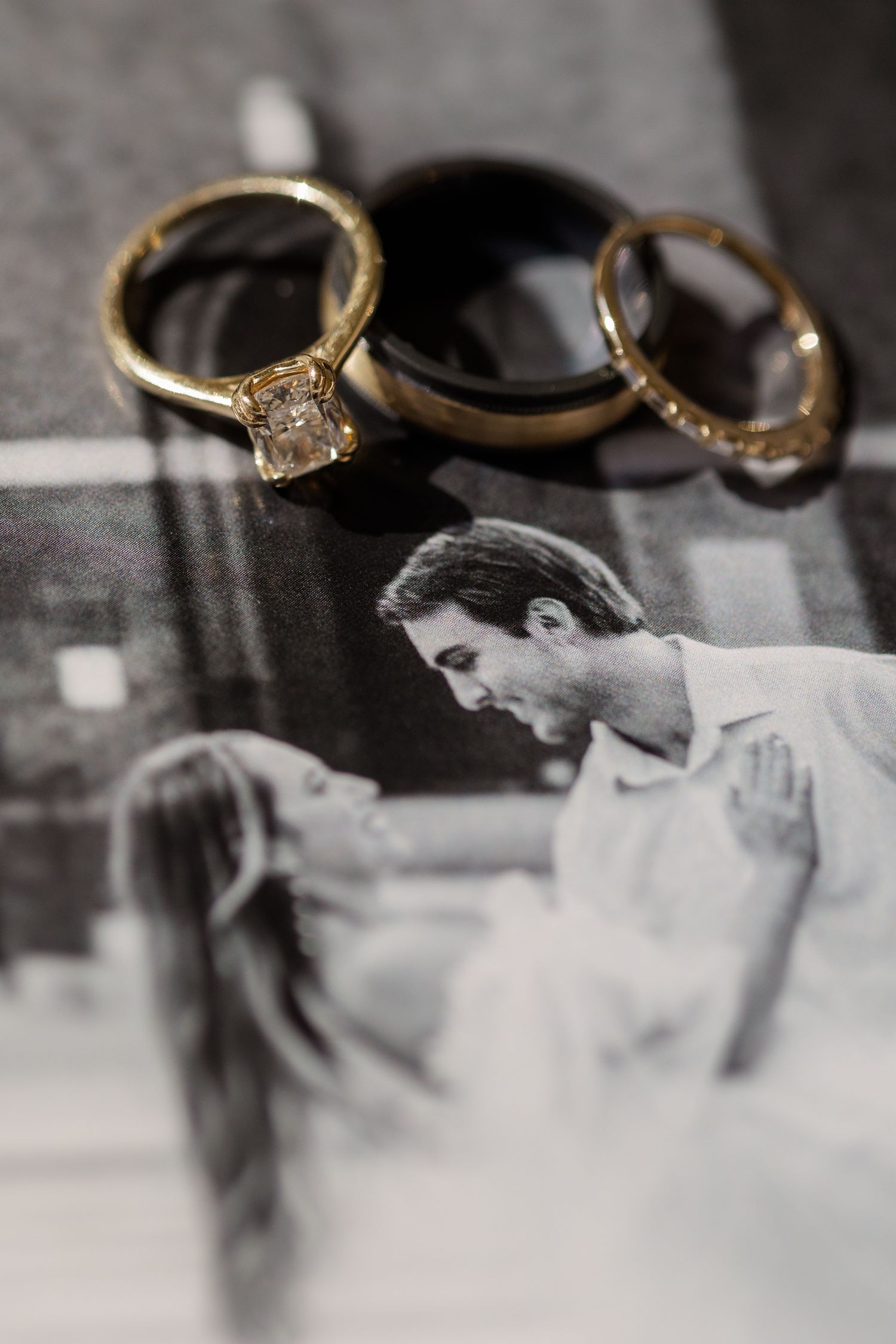 Wedding rings displayed above a black and white romantic photograph showing a tender couple moment. Destination Wedding Photographer