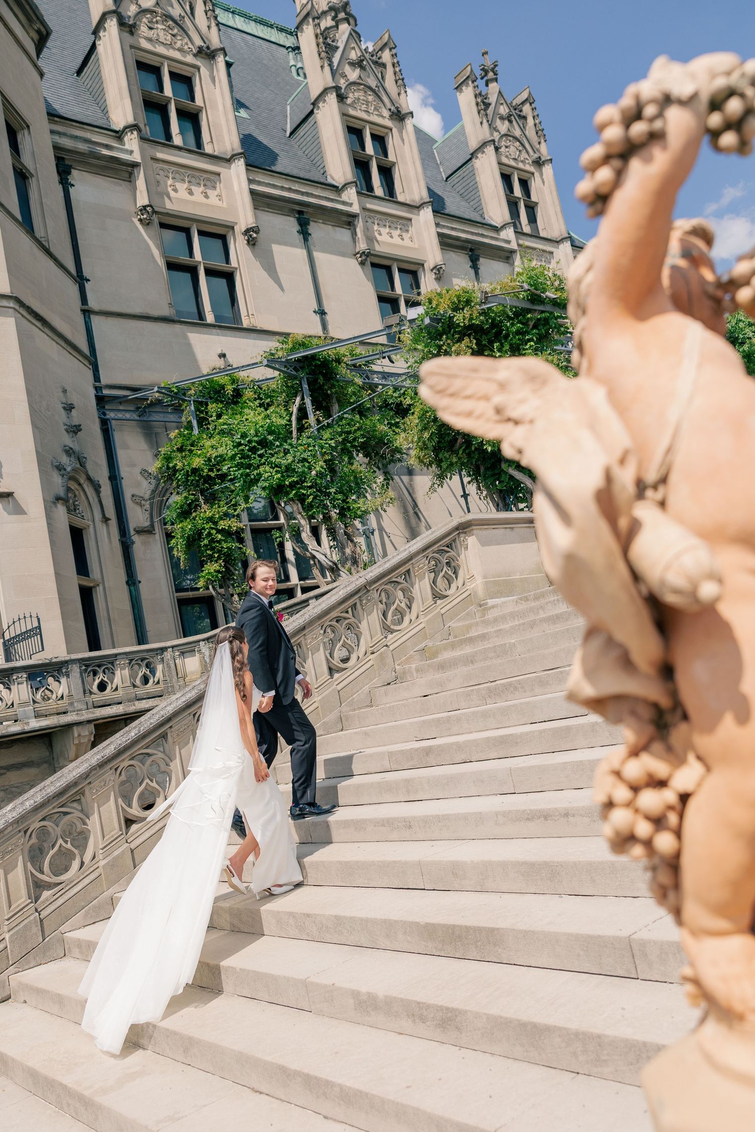 Bride and groom walking up ornate stone stairs at a grand historic estate on their wedding day.