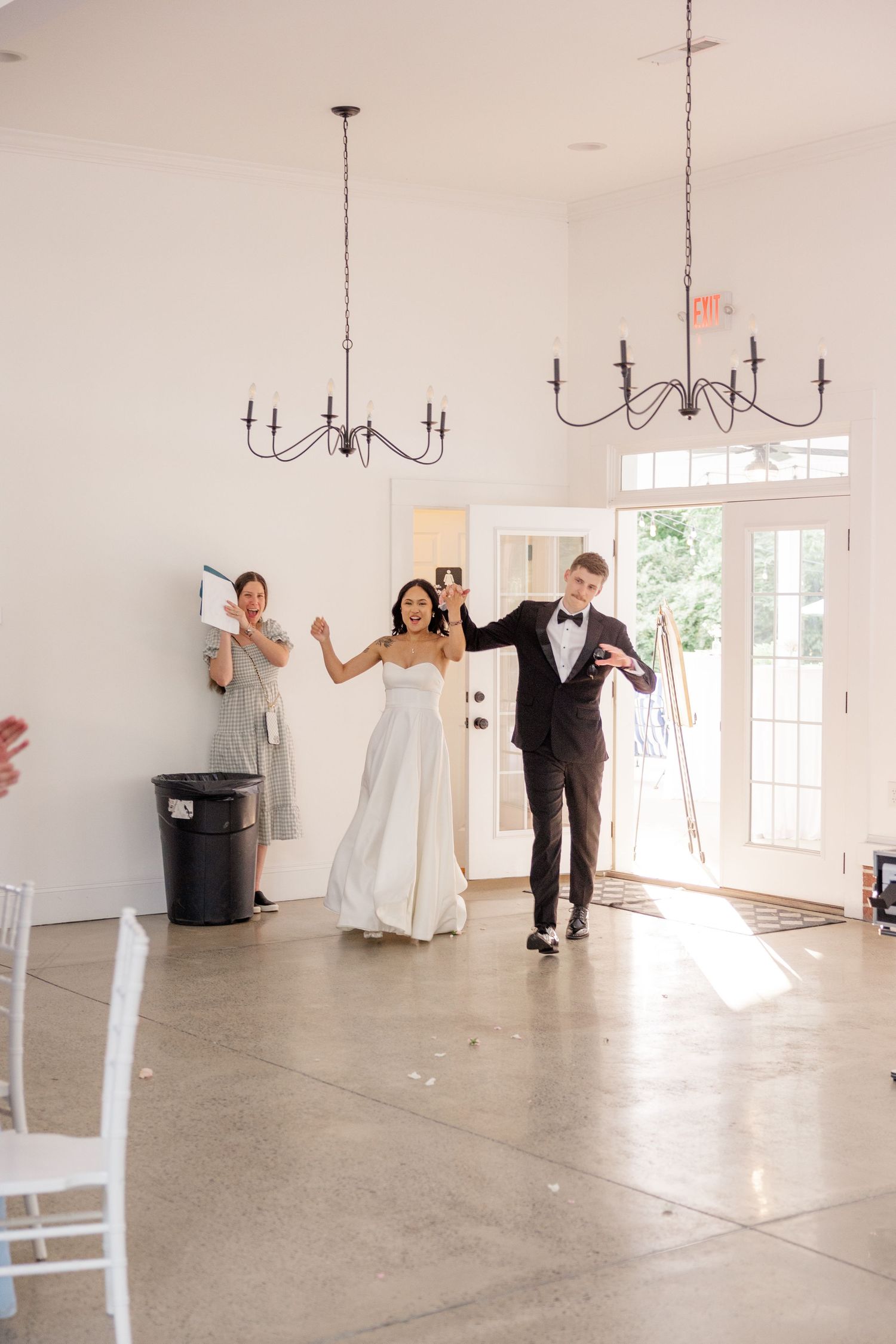 Wedding party makes grand entrance into bright reception venue with chandeliers.
