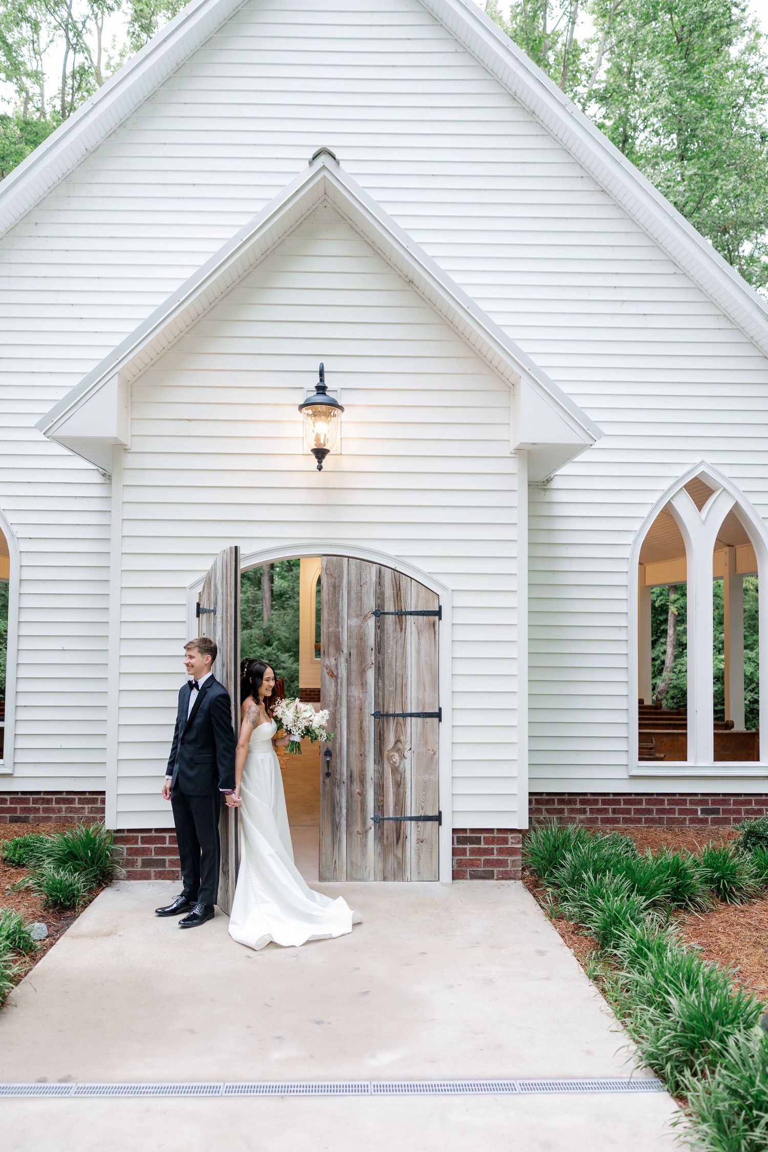Elegant white chapel wedding venue exterior with rustic wooden doors and Gothic-style windows.
