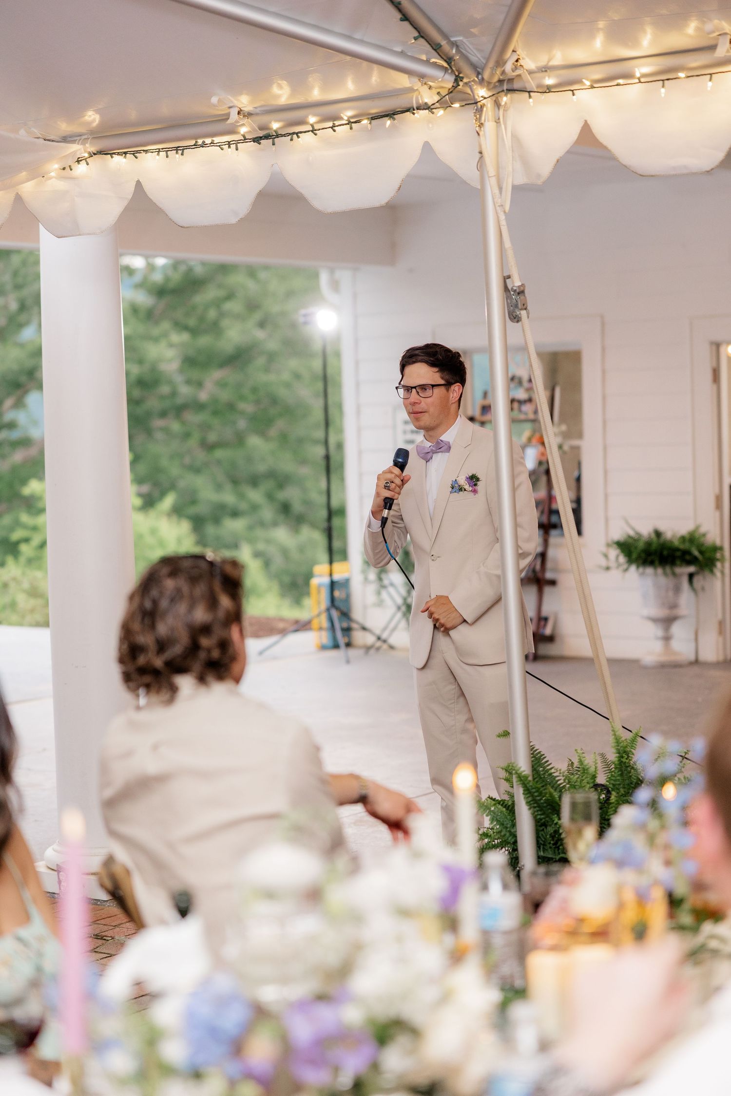 White tent wedding reception space decorated with string lights and paper lanterns.