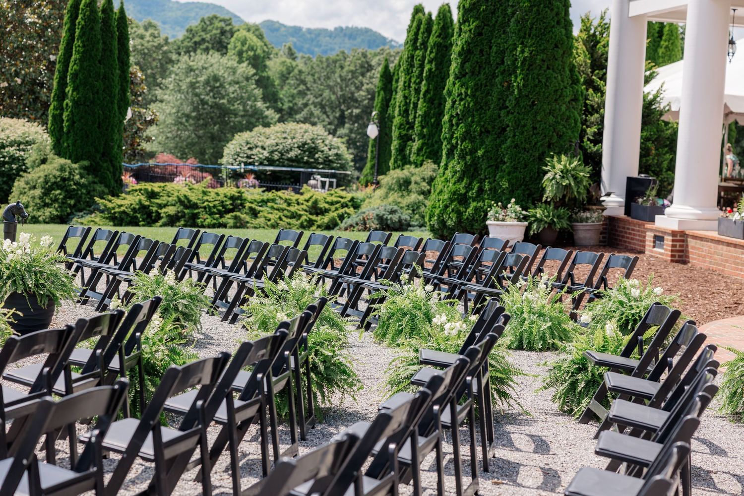 Rows of black chairs arranged for an outdoor wedding ceremony with mountain views and white columns.
