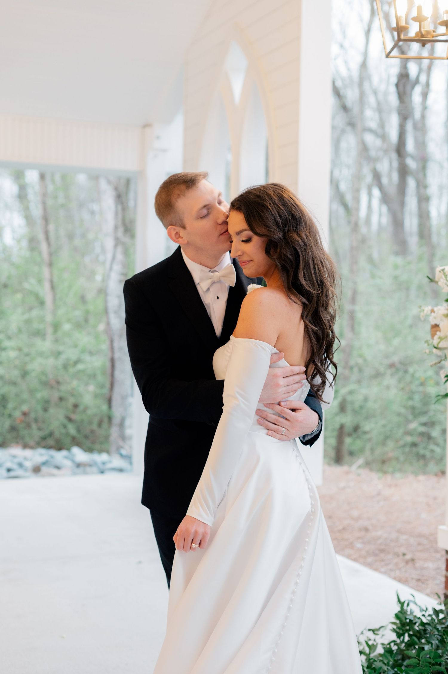 A romantic moment captured between newlyweds in a white chapel with natural light streaming through windows.