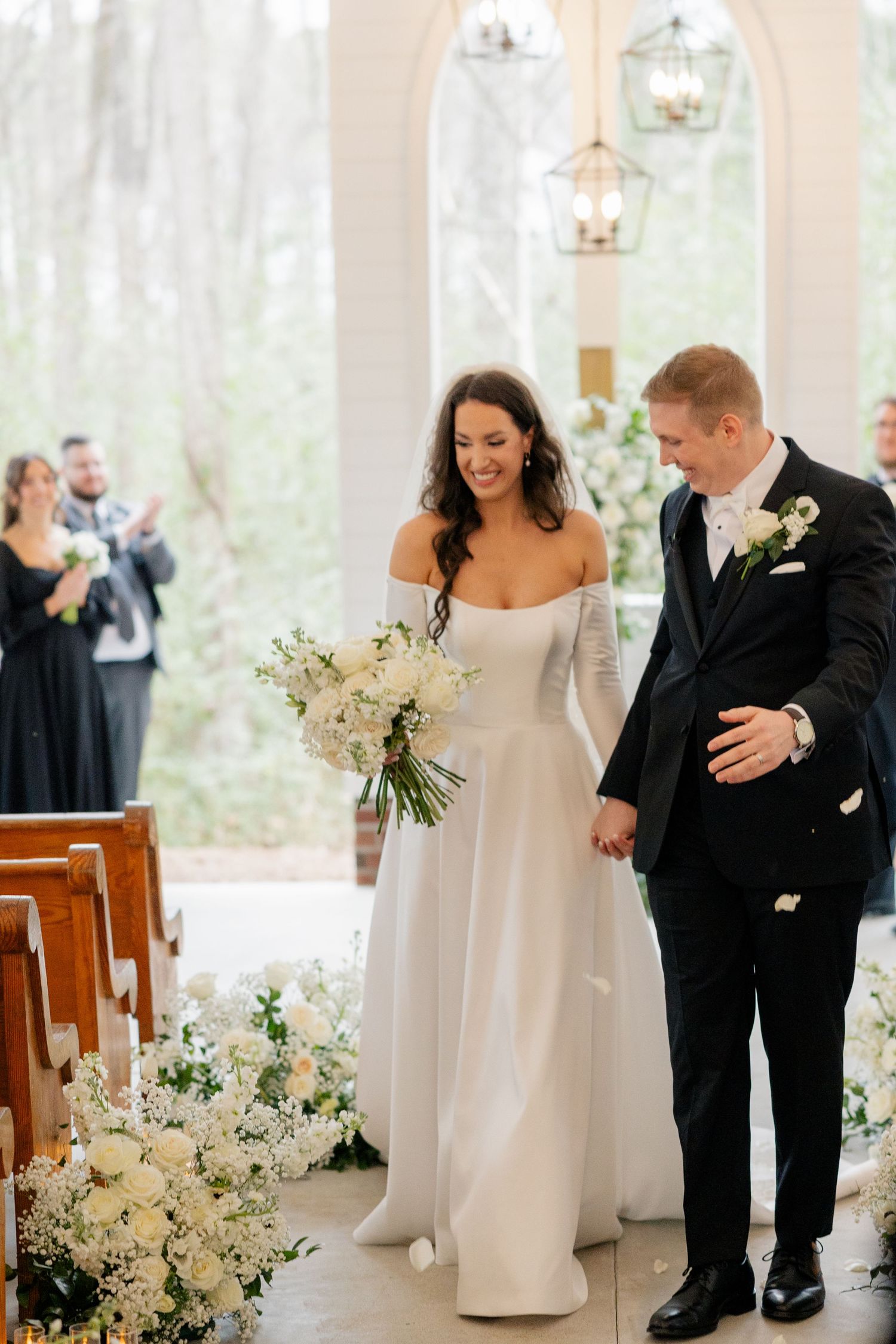Wedding couple celebrates joyfully after ceremony in a white chapel with floral decorations.