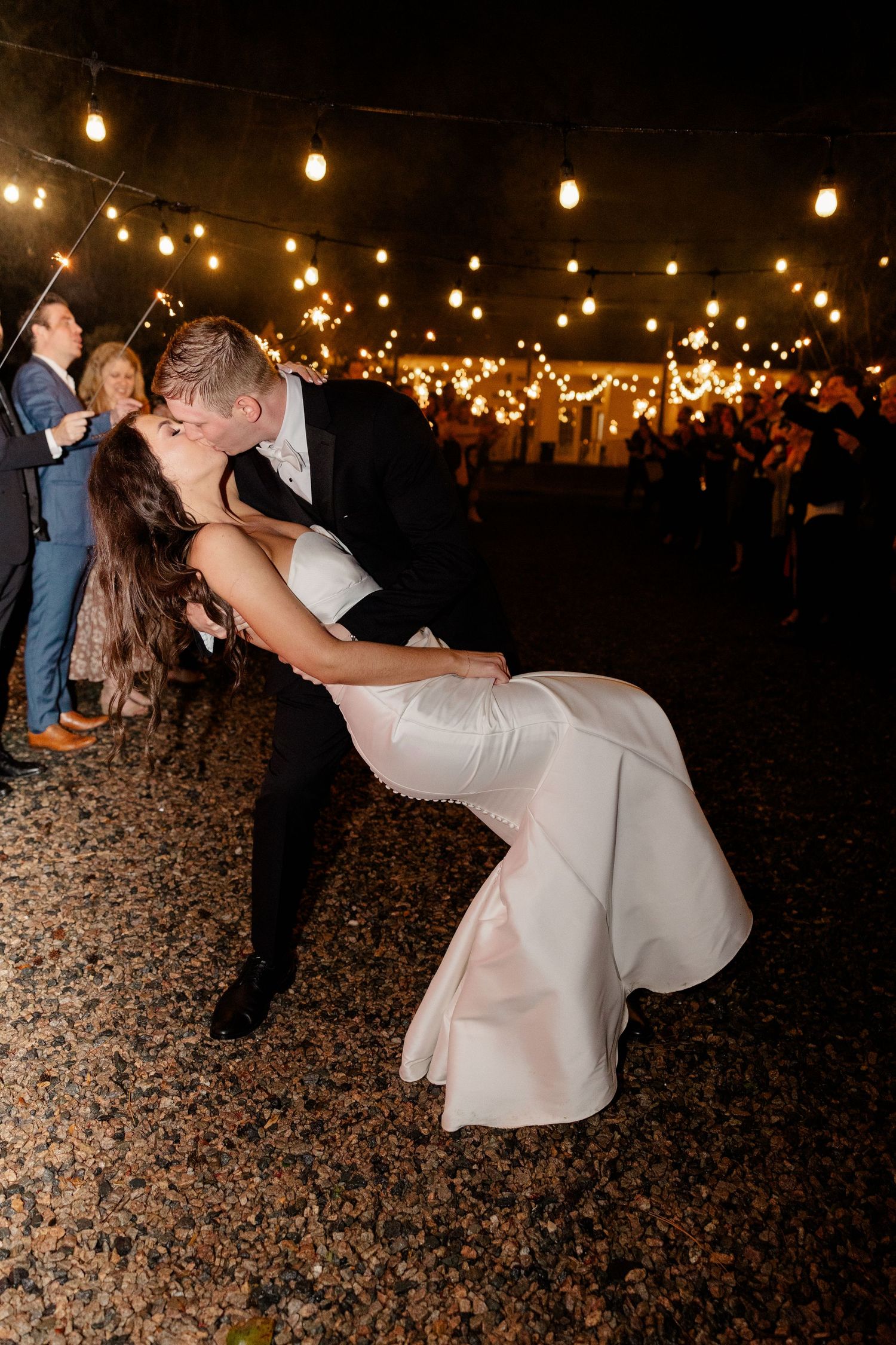 Romantic dip dance under string lights at an outdoor evening wedding reception.