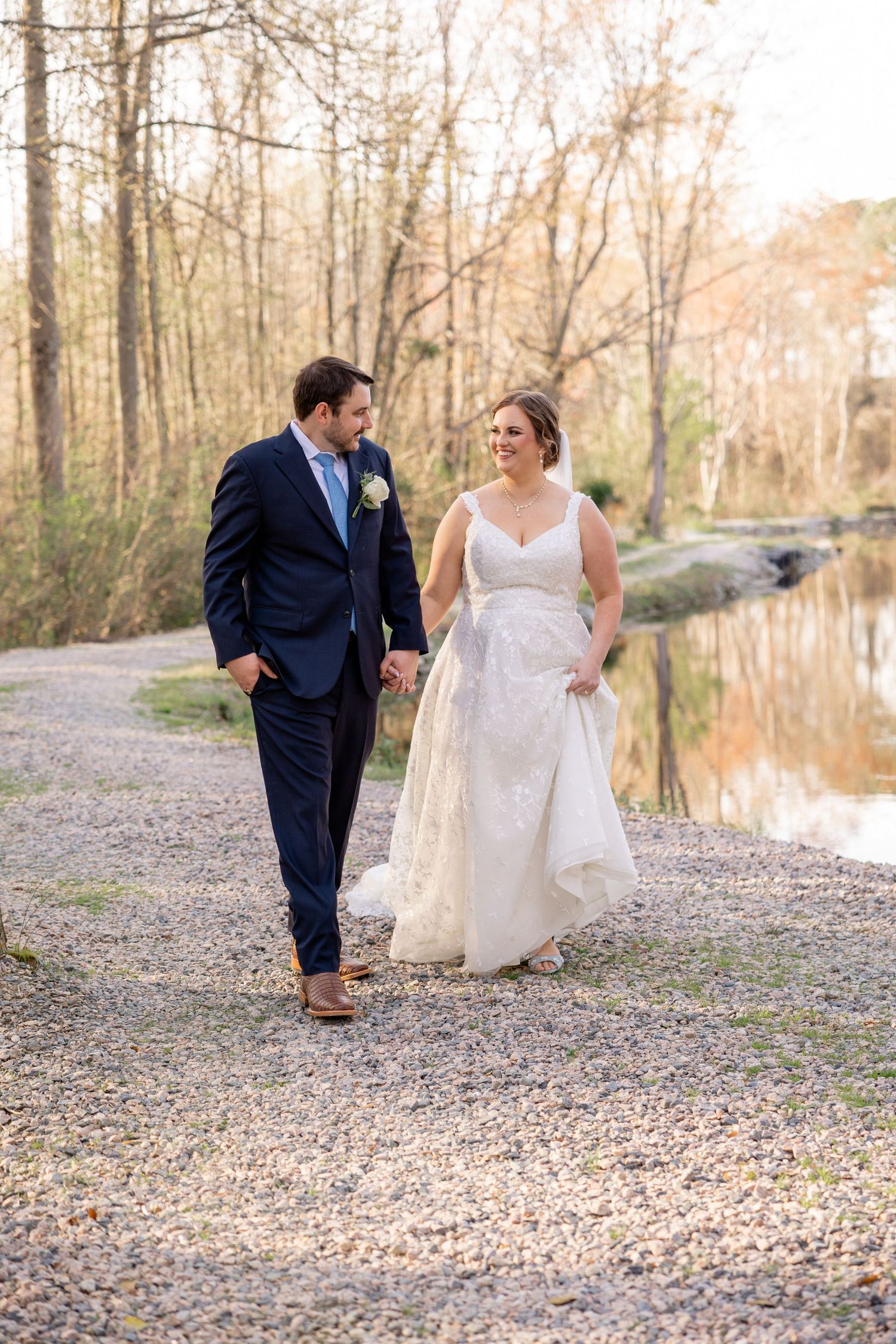 Wedding couple walking together on a gravel path near water.