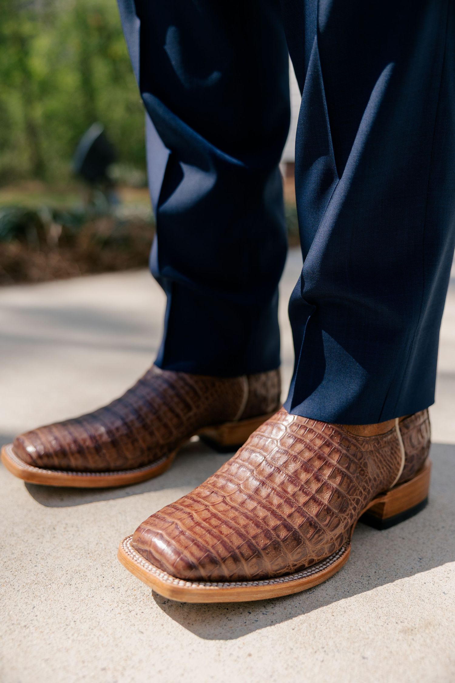 Brown leather alligator print dress shoes paired with navy suit pants at a formal event.