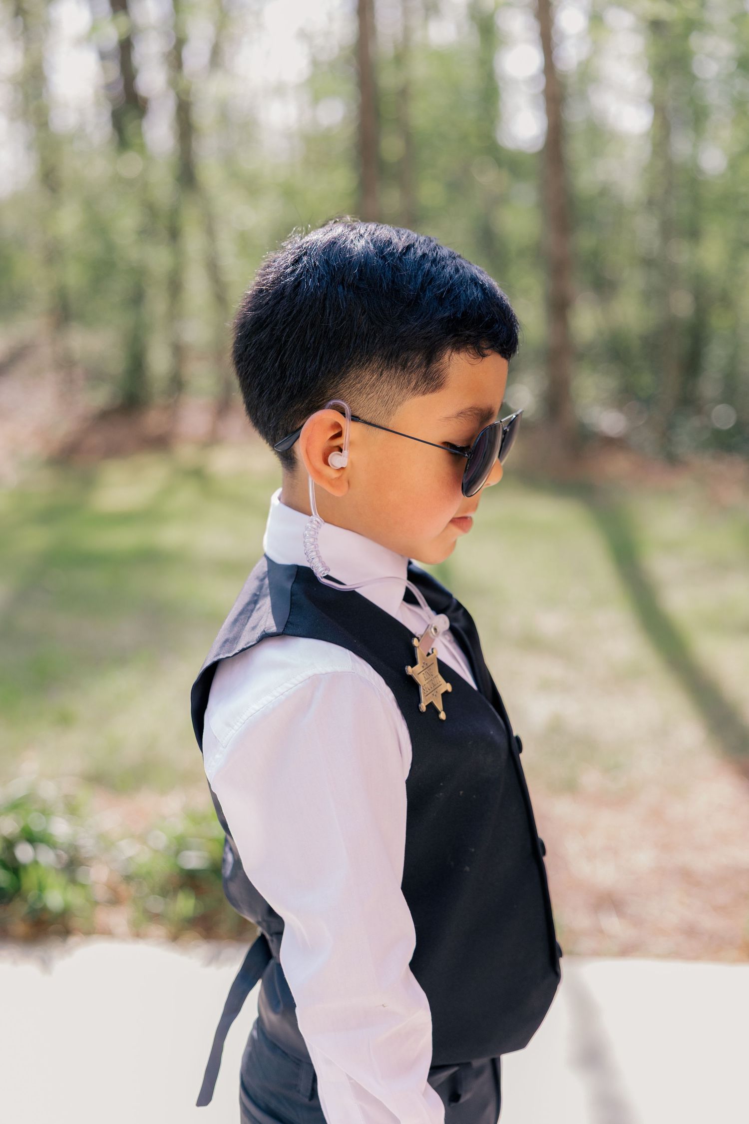 Young ring bearer in formal attire poses outdoors during wedding photo session.