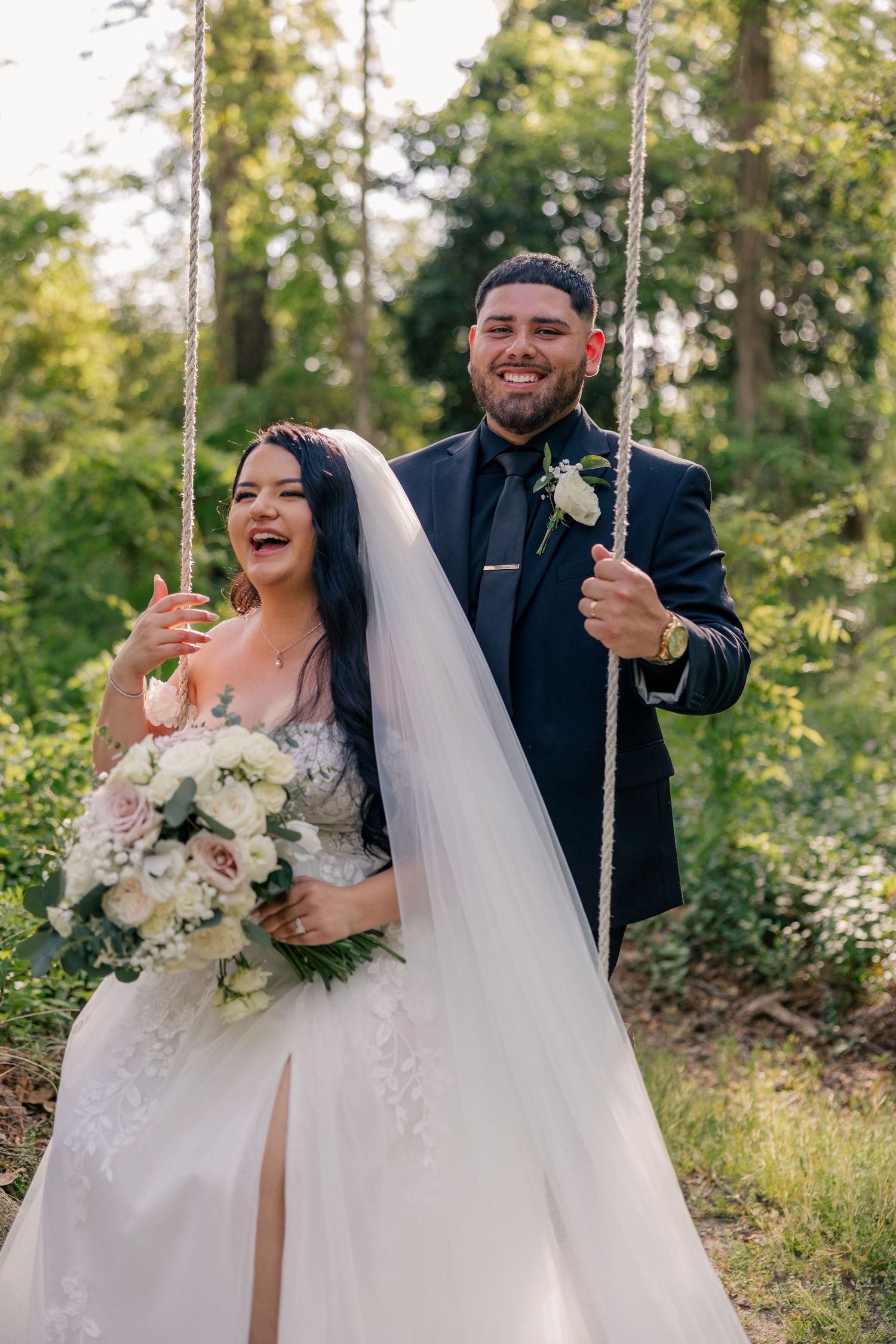 Wedding couple enjoying playful moments on a tree swing in a sunlit garden.