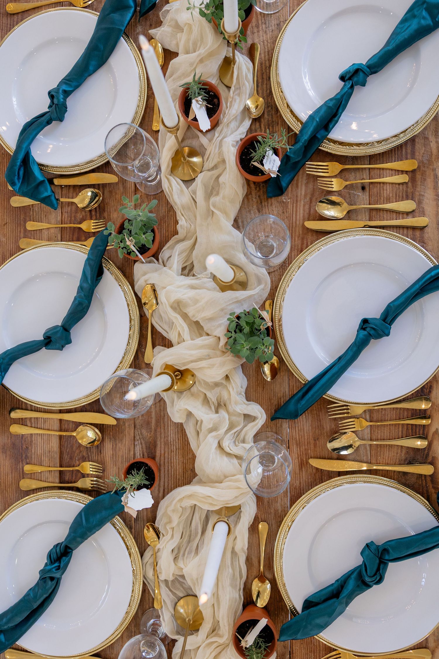 Elegant wedding table setting with teal napkins, gold cutlery, and white plates on a rustic wooden surface.