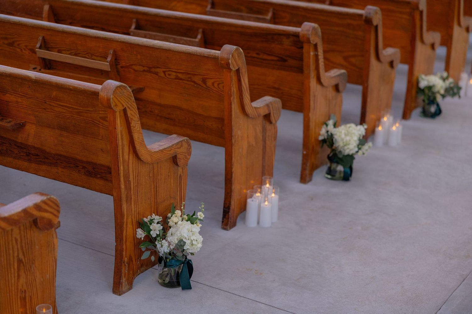 Church pews decorated with small floral arrangements in blue vases and white candles along the aisle.