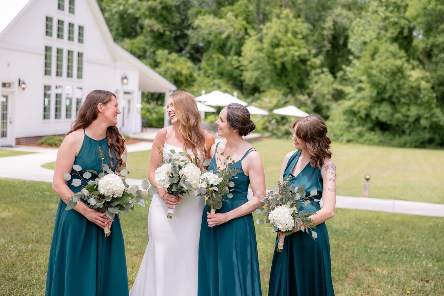 Wedding party in teal blue dresses standing outside a white chapel with bouquets of white flowers.