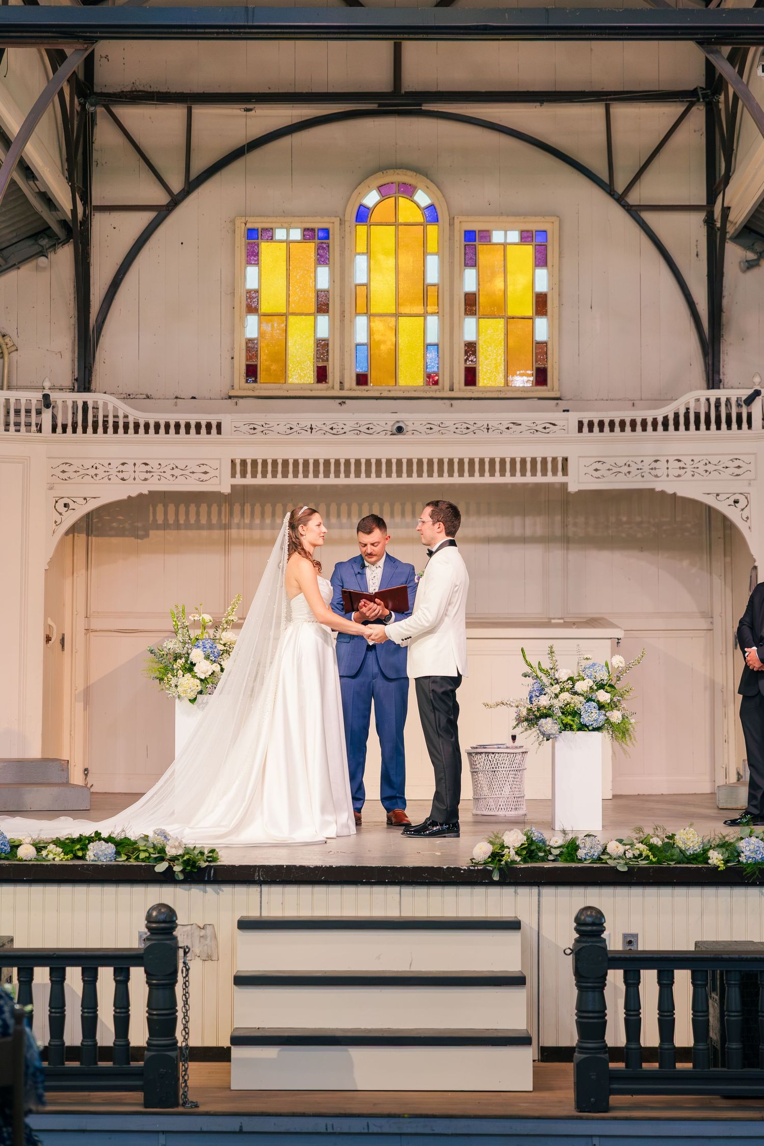 Bride and groom exchange vows at altar with stained glass windows and floral arrangements in elegant chapel.