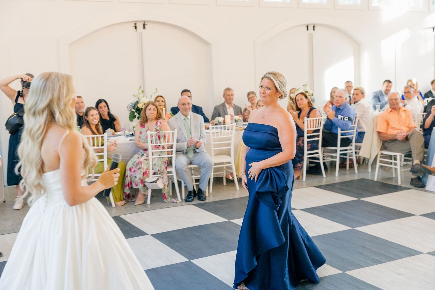 Bridesmaid in navy blue gown faces bride on black and white checkered dance floor at reception.