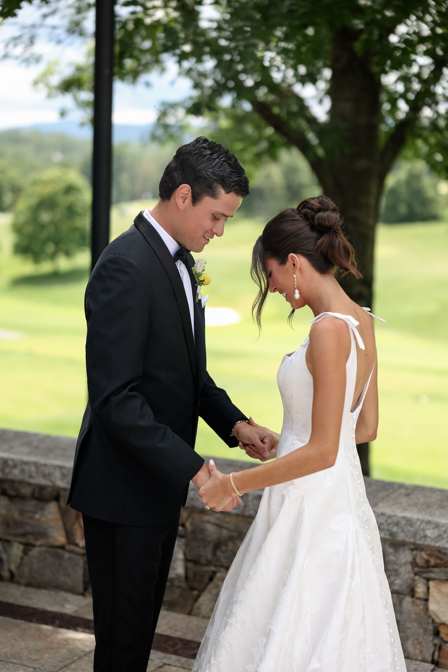 Bride and groom holding hands during wedding ceremony on stone terrace with lush green golf course background.