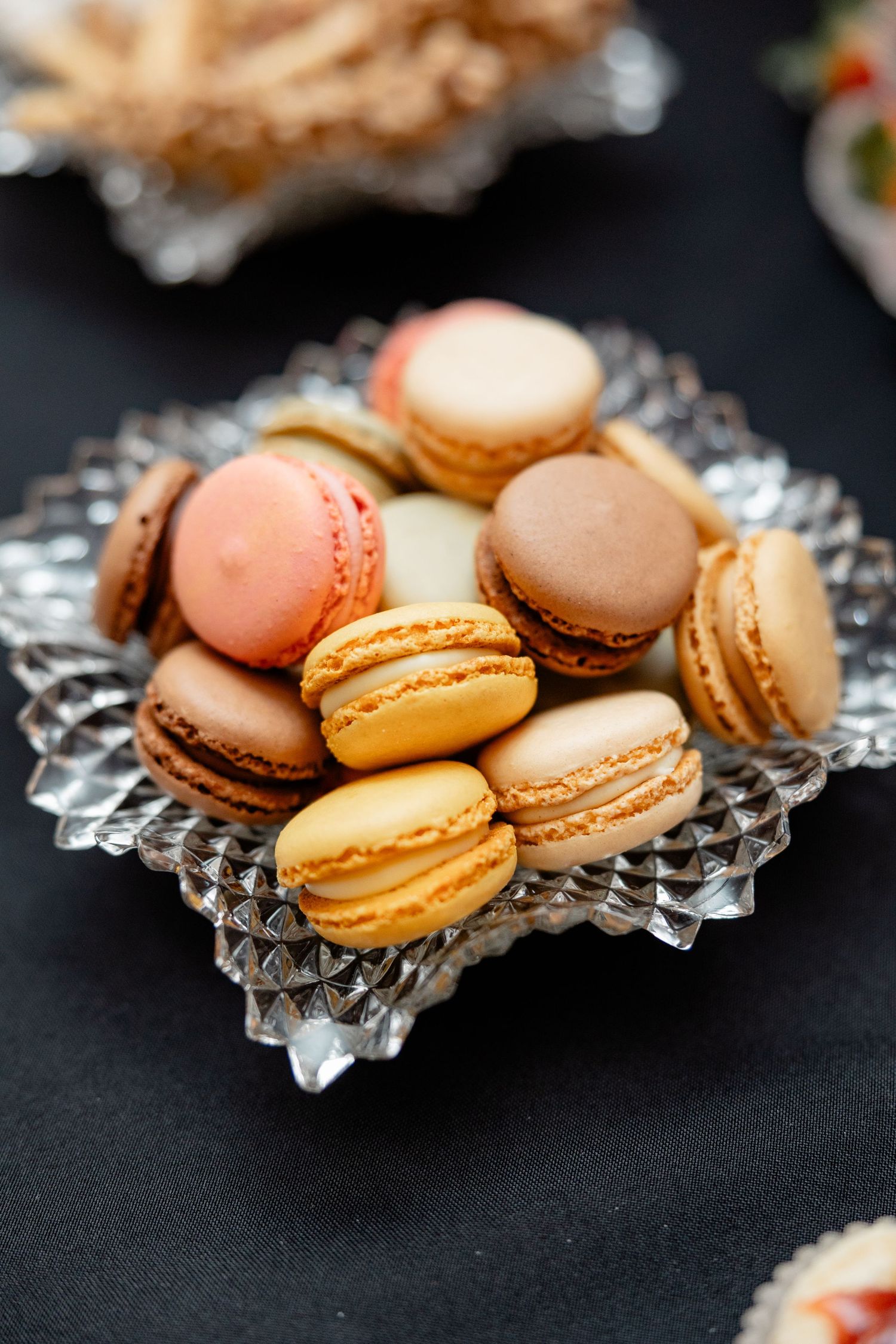 Colorful French macarons in pastel shades displayed on a crystal serving dish against a dark background.