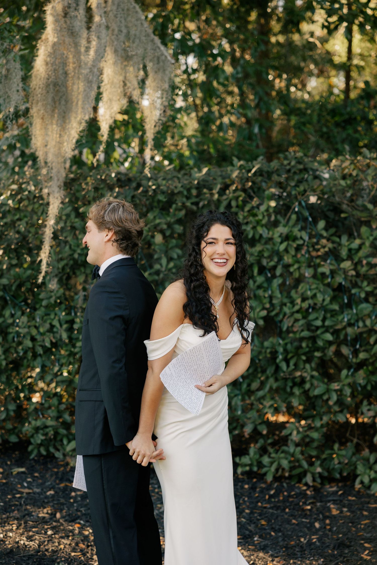 A couple shares a joyful first look moment in a garden setting with Spanish moss hanging overhead.