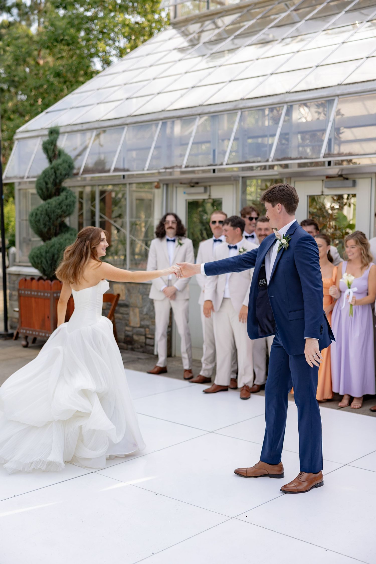 Wedding party dancing and celebrating on a white dance floor next to a greenhouse.