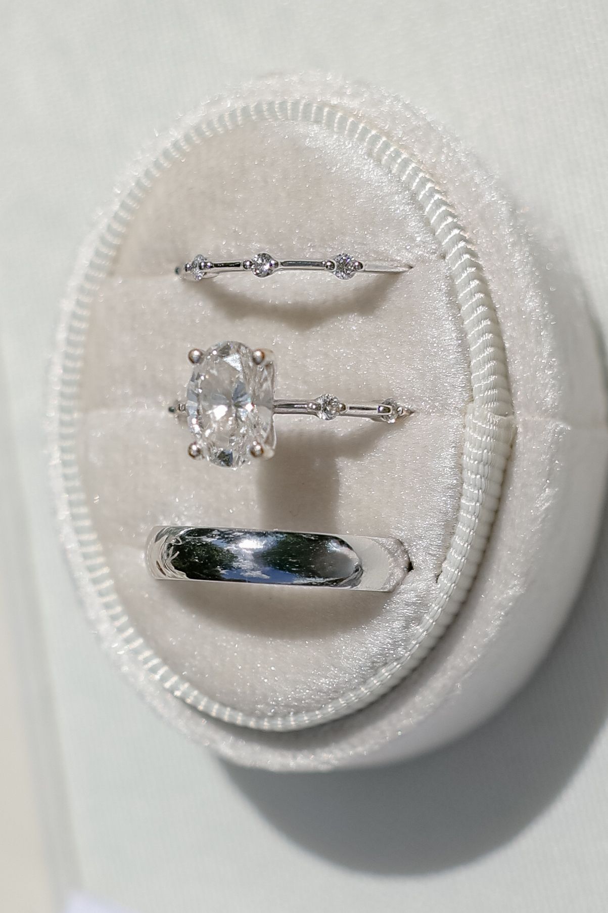 Four identical white ring cushions display delicate silver engagement rings with diamond accents and matching bands.
