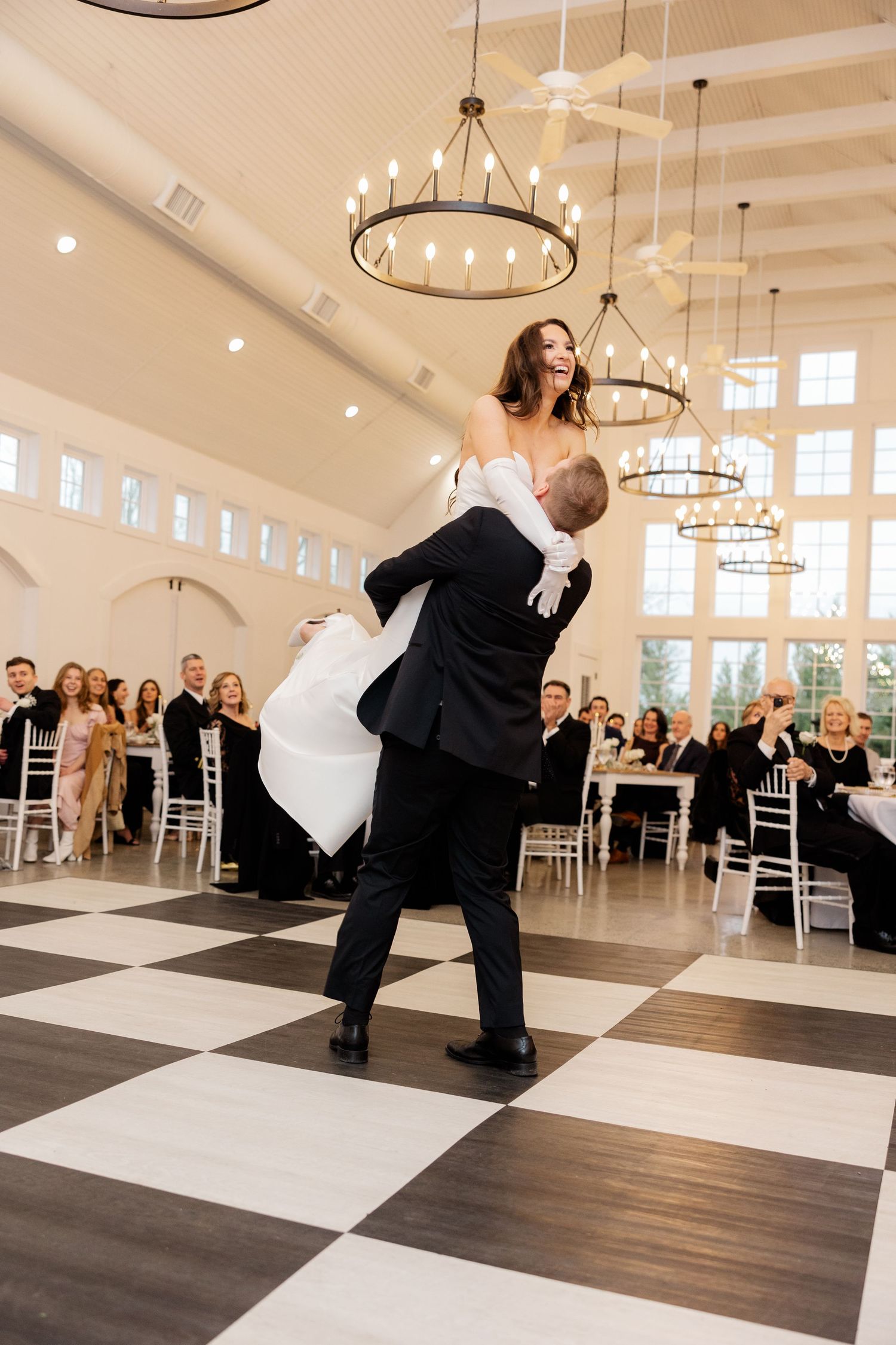 Wedding couple performs dramatic dip dance move on black and white checkered floor.
