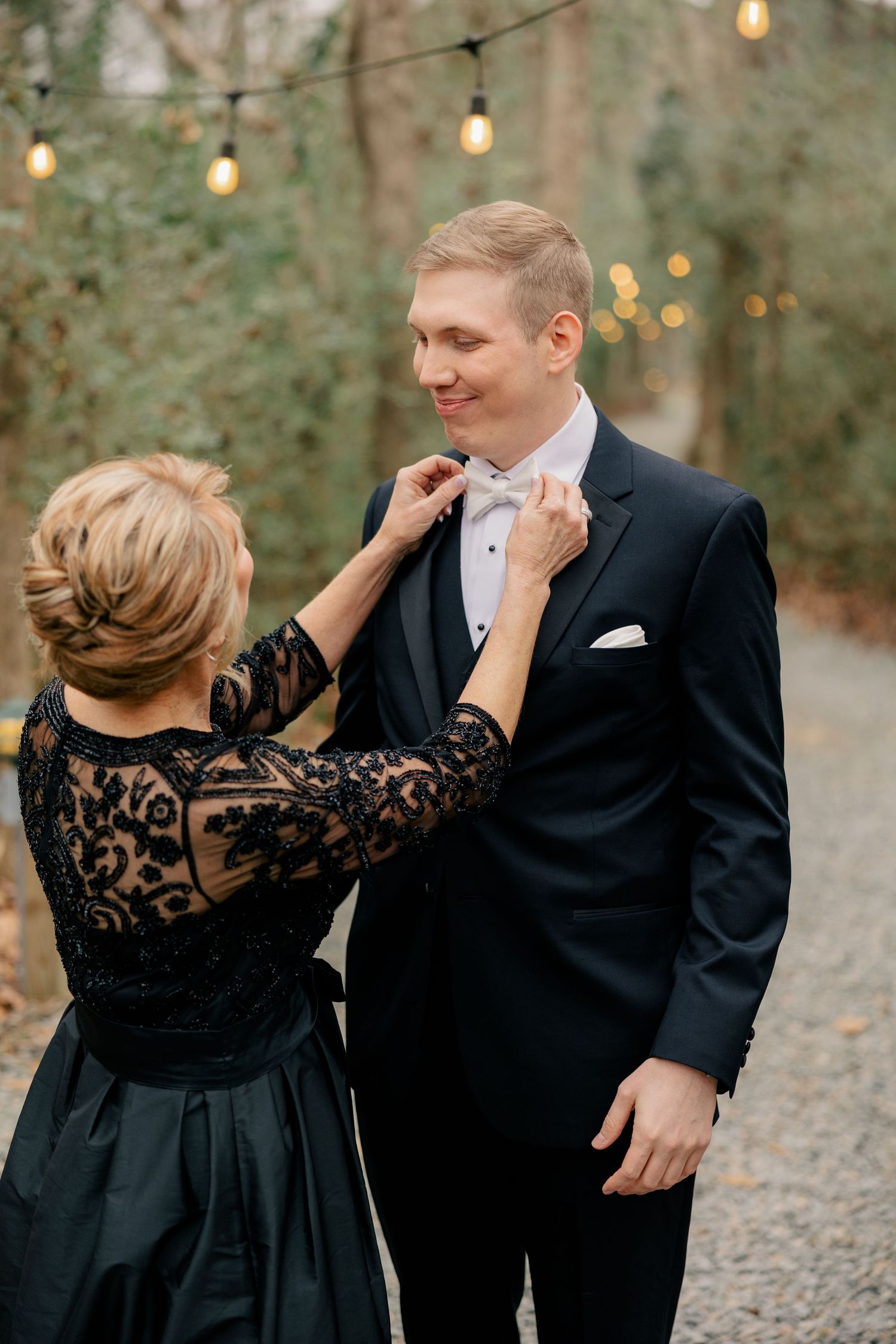 A romantic first look moment between a couple with string lights glowing in a wooded outdoor setting.