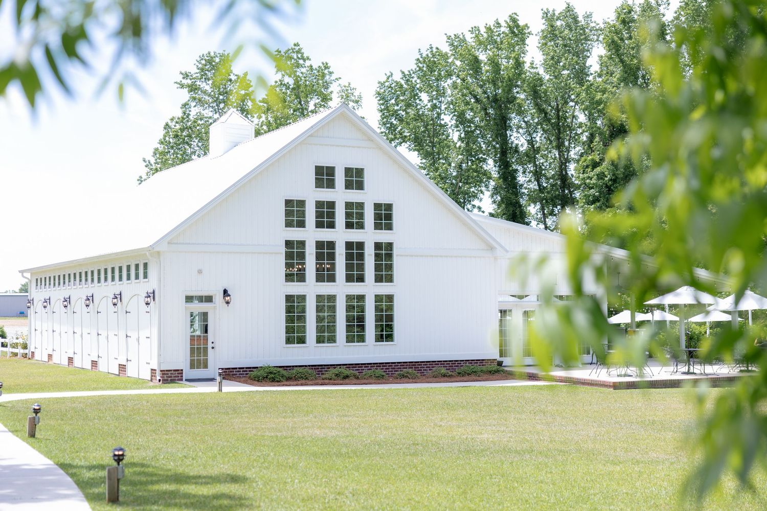 Large white barn-style wedding venue with glass windows and manicured lawn surrounded by trees.