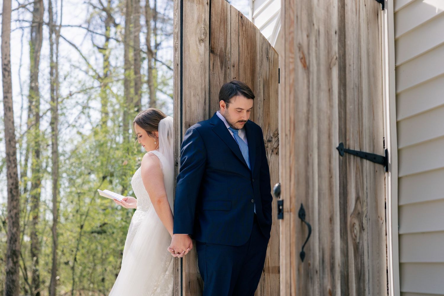 A couple shares a private first look moment behind a rustic wooden door.