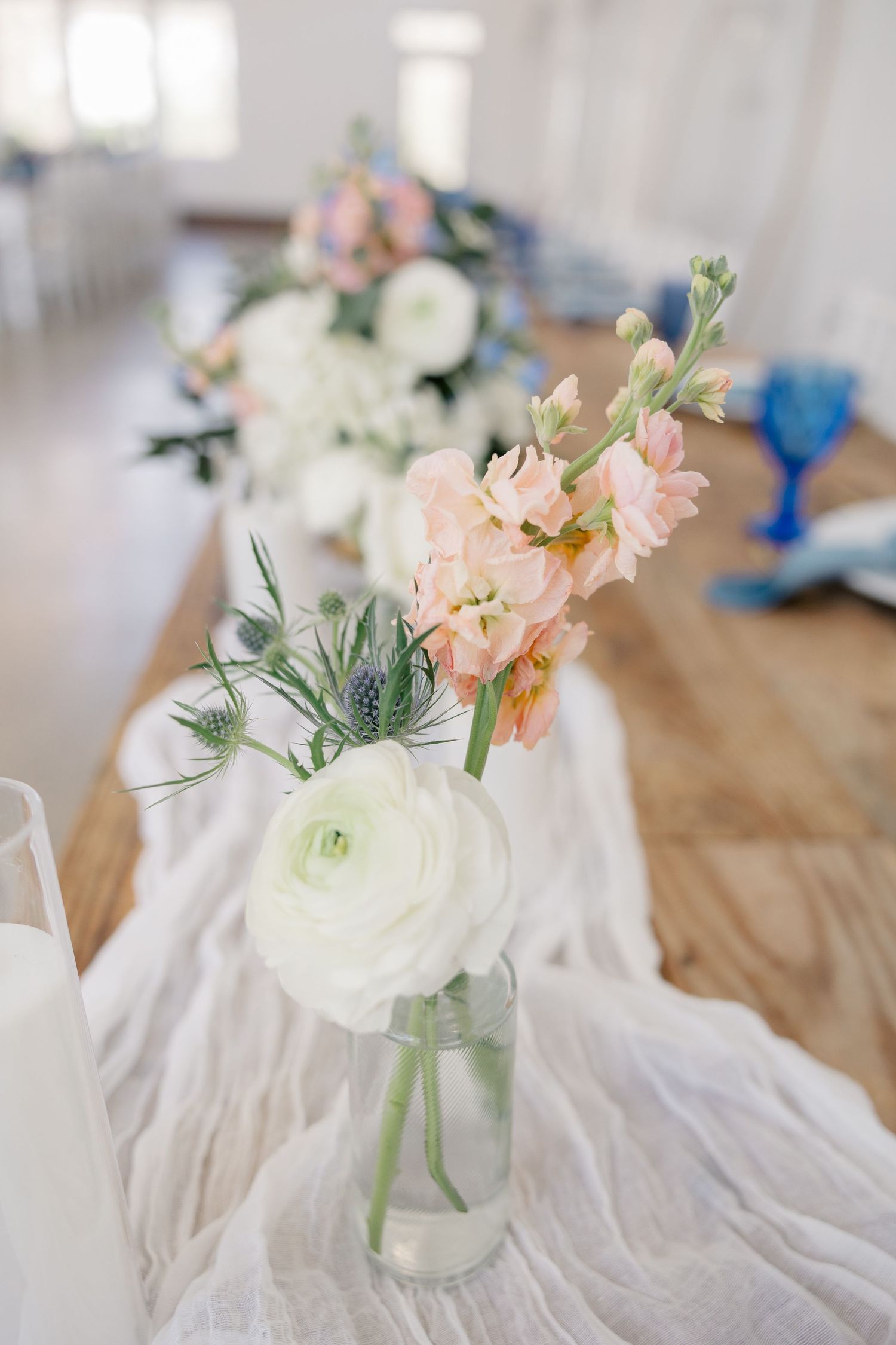 Simple floral centerpieces with blush and white flowers in glass vases on white fabric.