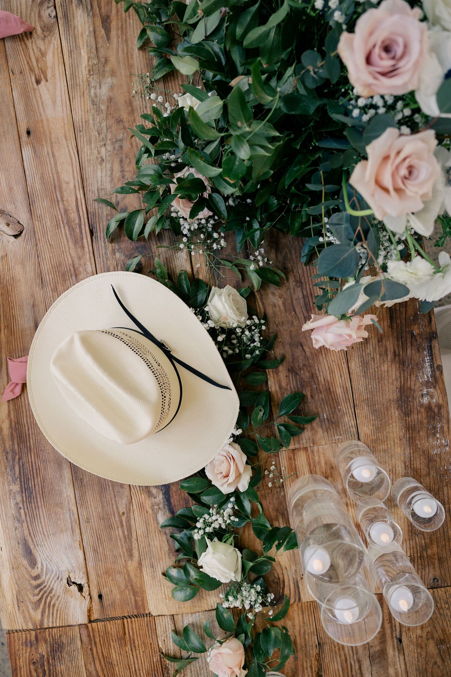 Wedding decor featuring white cowboy hats, pink roses and wooden backdrop at rustic venue.